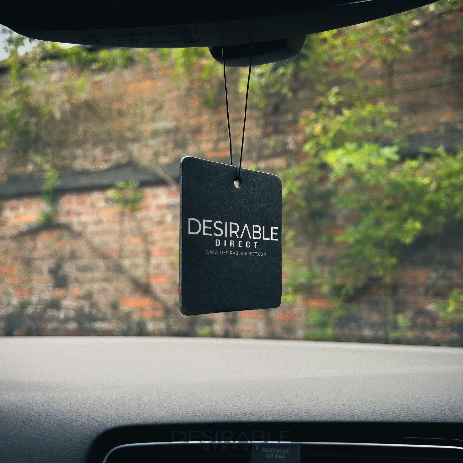 Car care black car air freshener with desirable direct and desirabledirect.com printed on the front, hanging in the front of a volkswagen golf r.