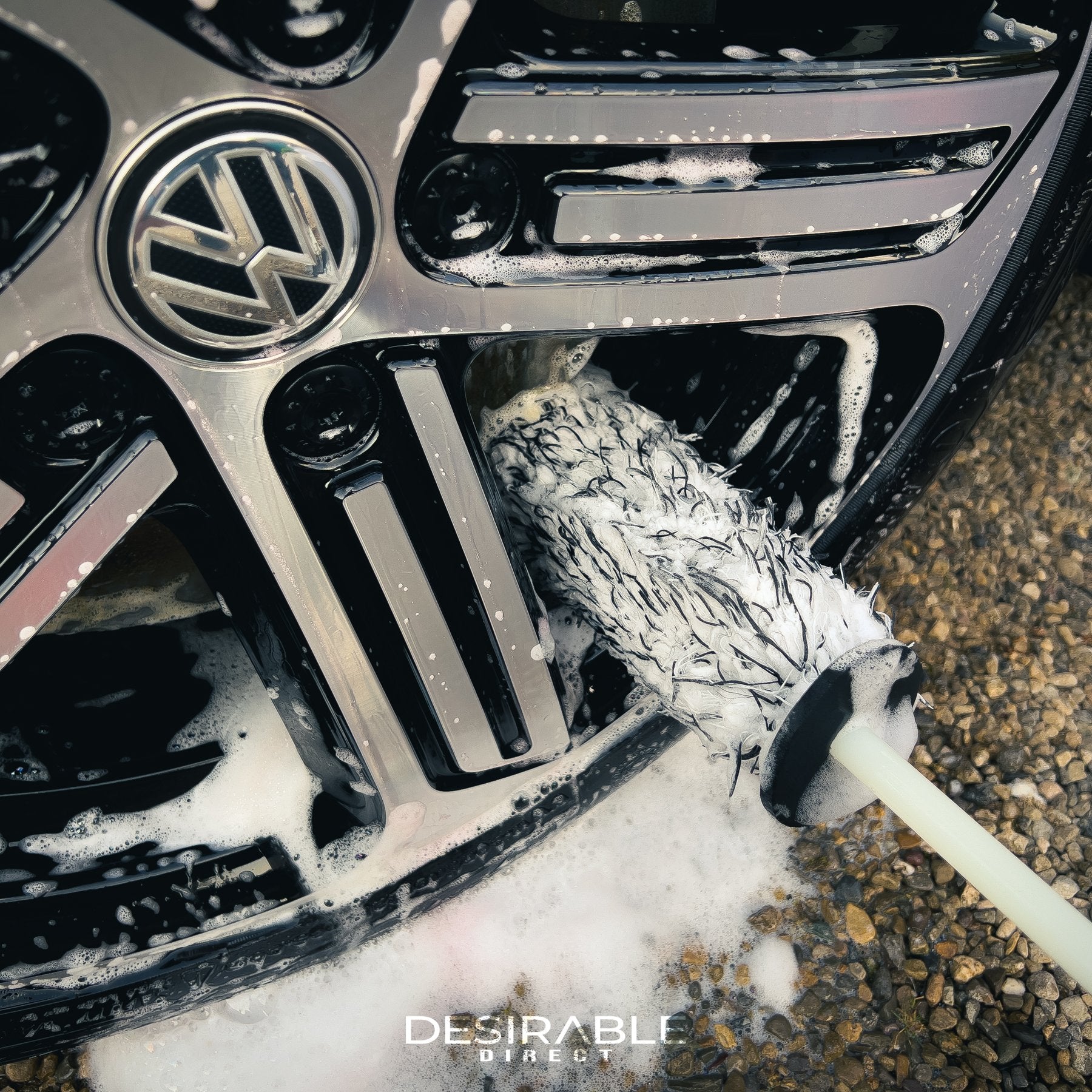 Car care microfibre black and white alloy wheel brush cleaning the bottom section of a silver alloy wheel on a blue volkswagen golf r.