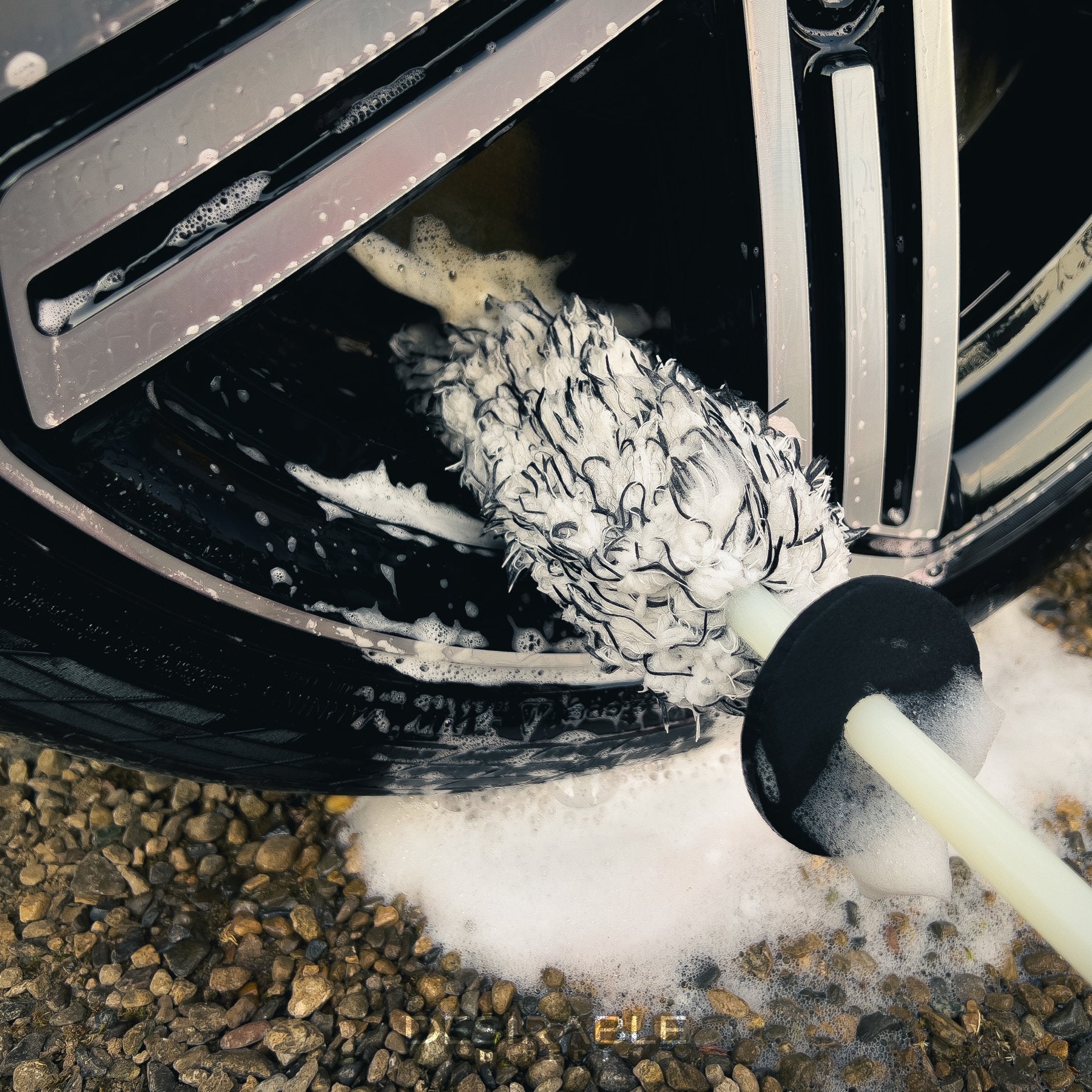 Car care microfibre black and white alloy wheel brush cleaning the bottom section of a silver alloy wheel on a blue volkswagen golf r. This is a close-up photo showing the wheel brush.