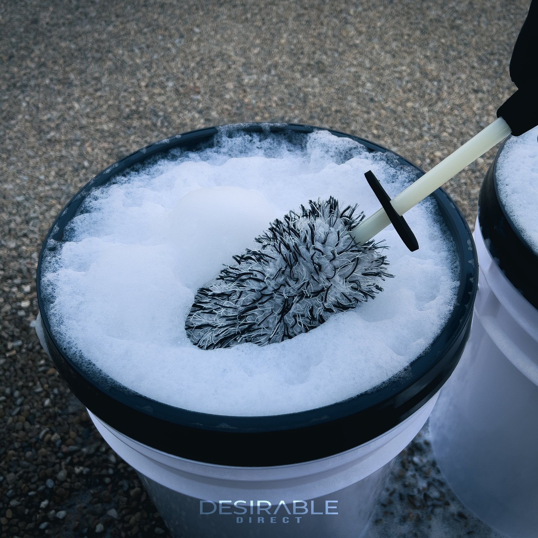 Car care microfibre black and white alloy wheel brush submerged in a car cleaning bucket filled with water and car shampoo.