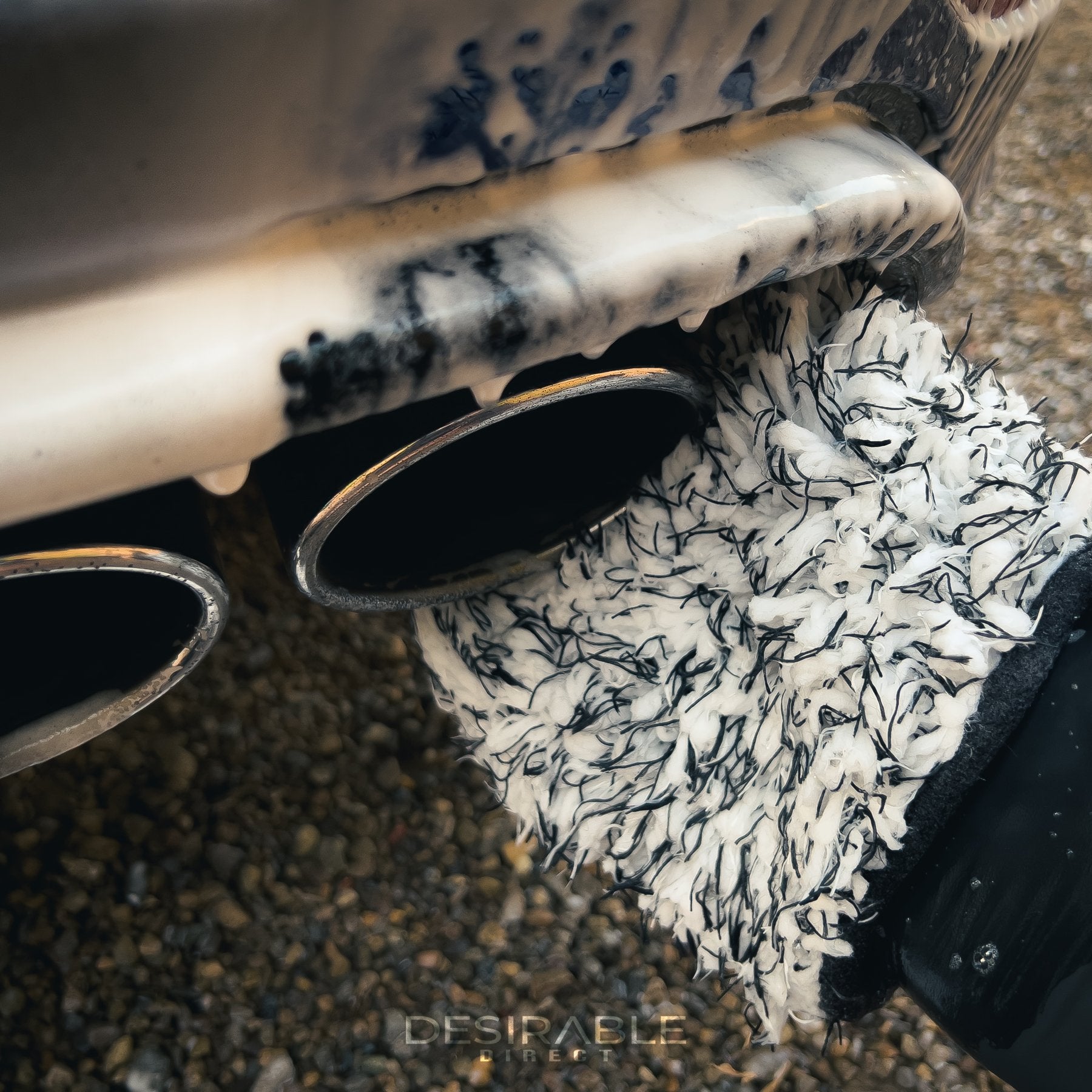 Car care microfibre black and white wheel and trim wash mitt cleaning the chrome exhausts on a blue volkswagen golf r. The car is covered in car shampoo.