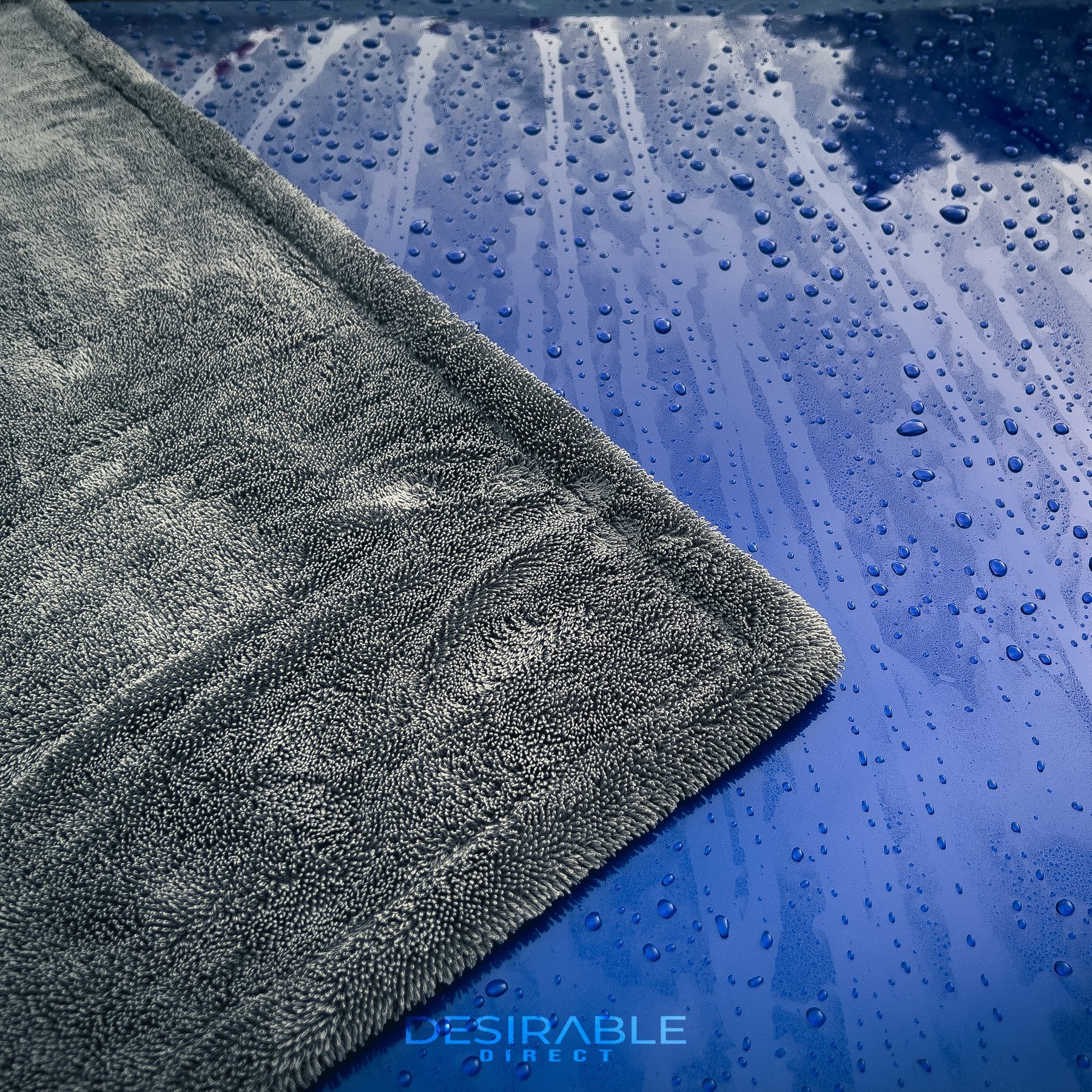 Car care large twisted pile grey drying towel displayed on the bonnet of a blue volkswagen golf r. The vehicle is wet to showcase the drying capability of the towel and the photo is a close-up to show the towel and the water on the paintwork.