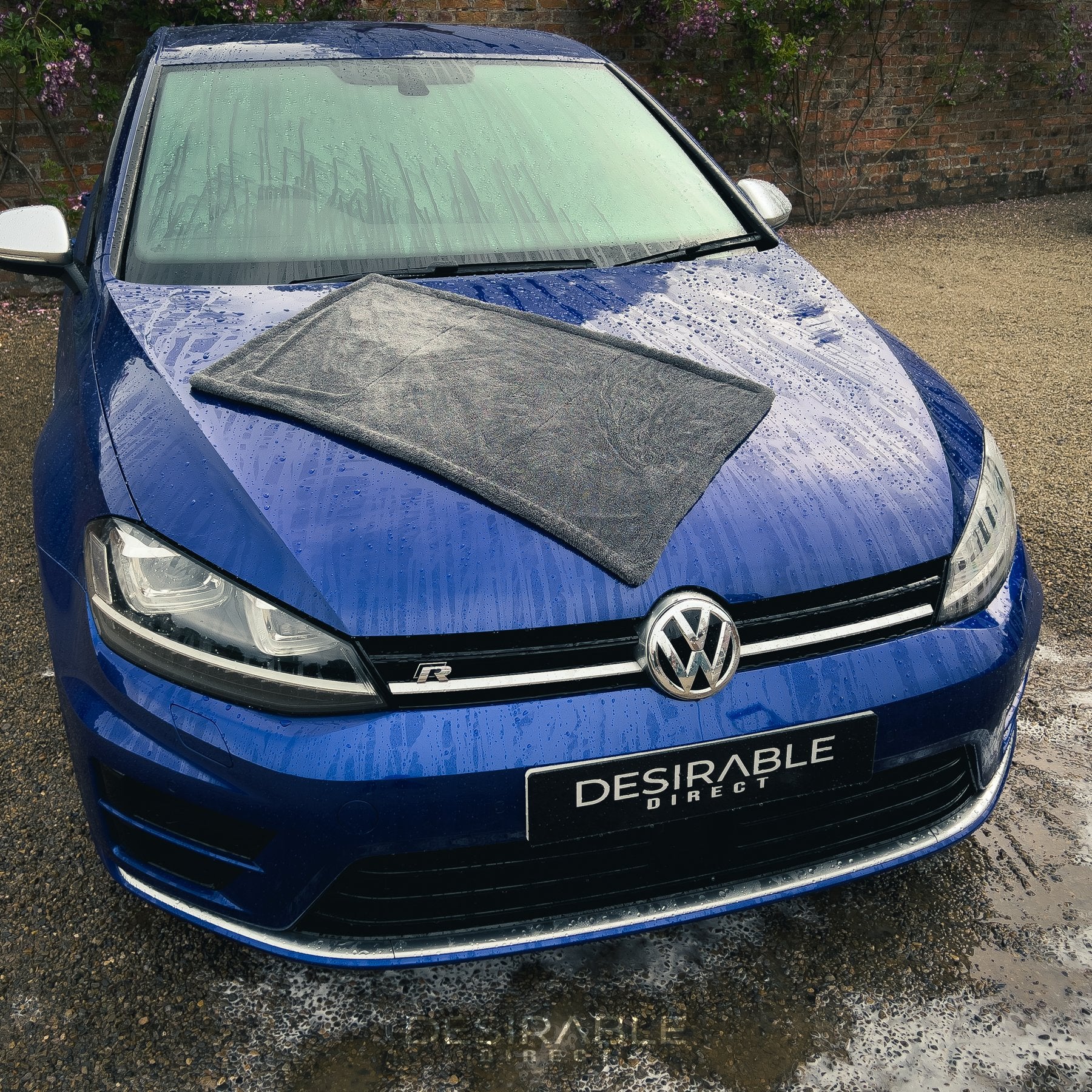 Car care large twisted pile grey drying towel displayed on the bonnet of a blue volkswagen golf r. The vehicle is wet to showcase the drying capability of the towel. The photo is taken from the front of the vehicle.