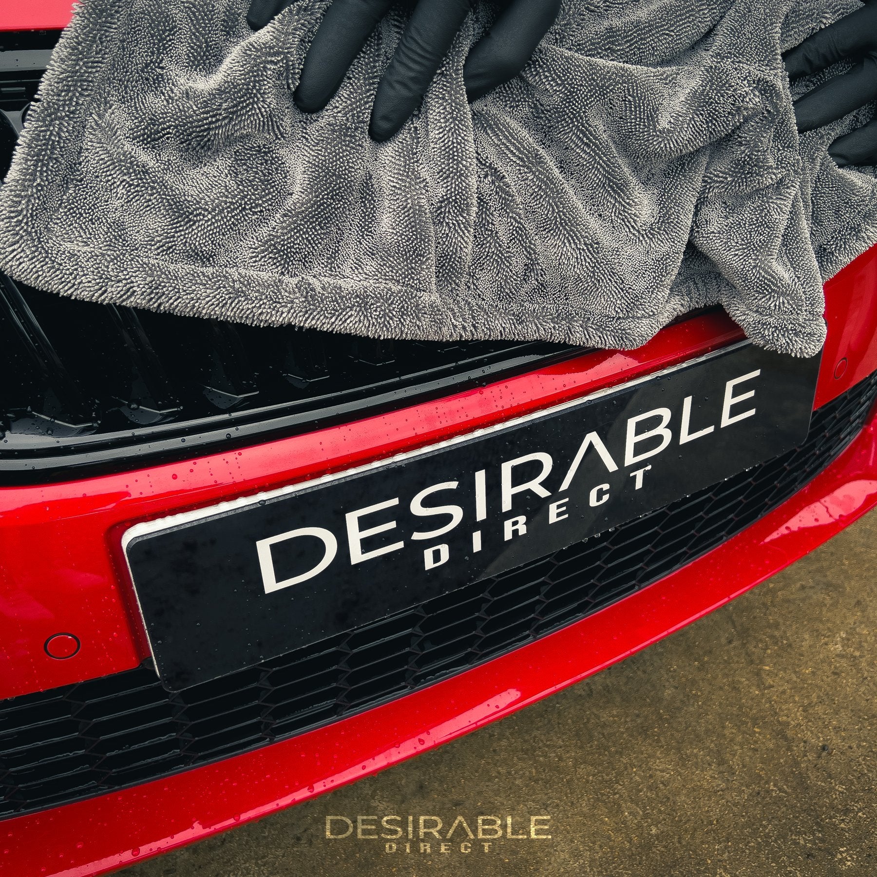 Car care large twisted pile grey drying towel drying a wet red car. Somebody is holding the towel while drying the front of the car wearing black gloves.
