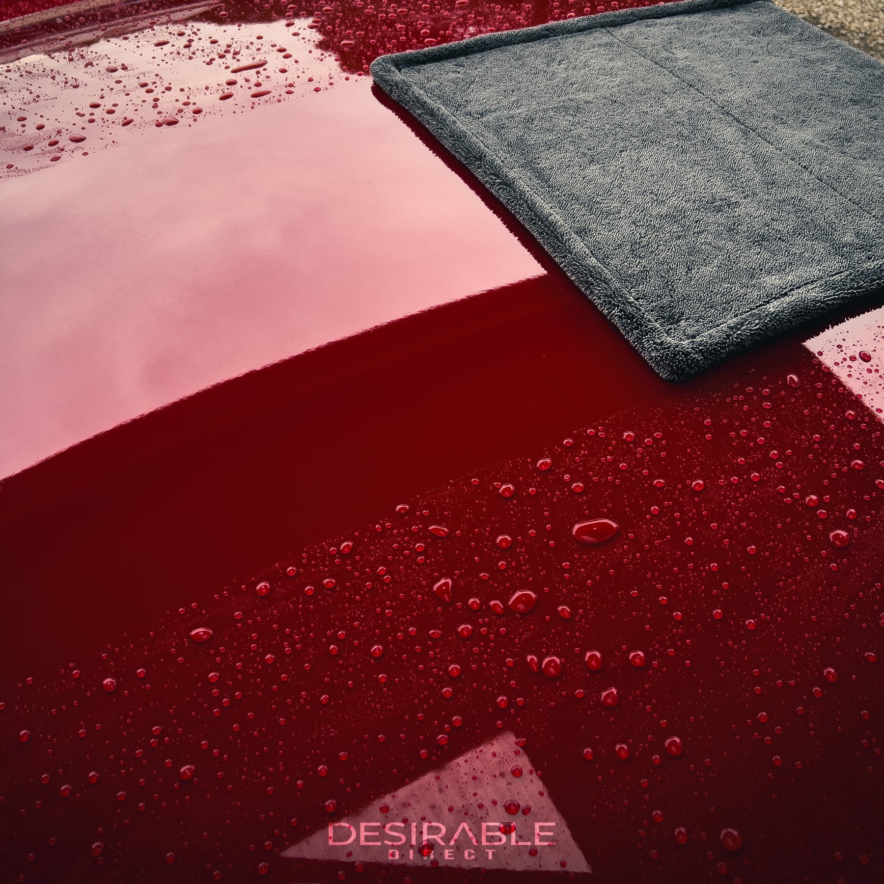 Car care large twisted pile grey drying towel showcased on the roof of a red car covered in water. The photo shows the performance of the towel as it has absorbed the water on the roof.