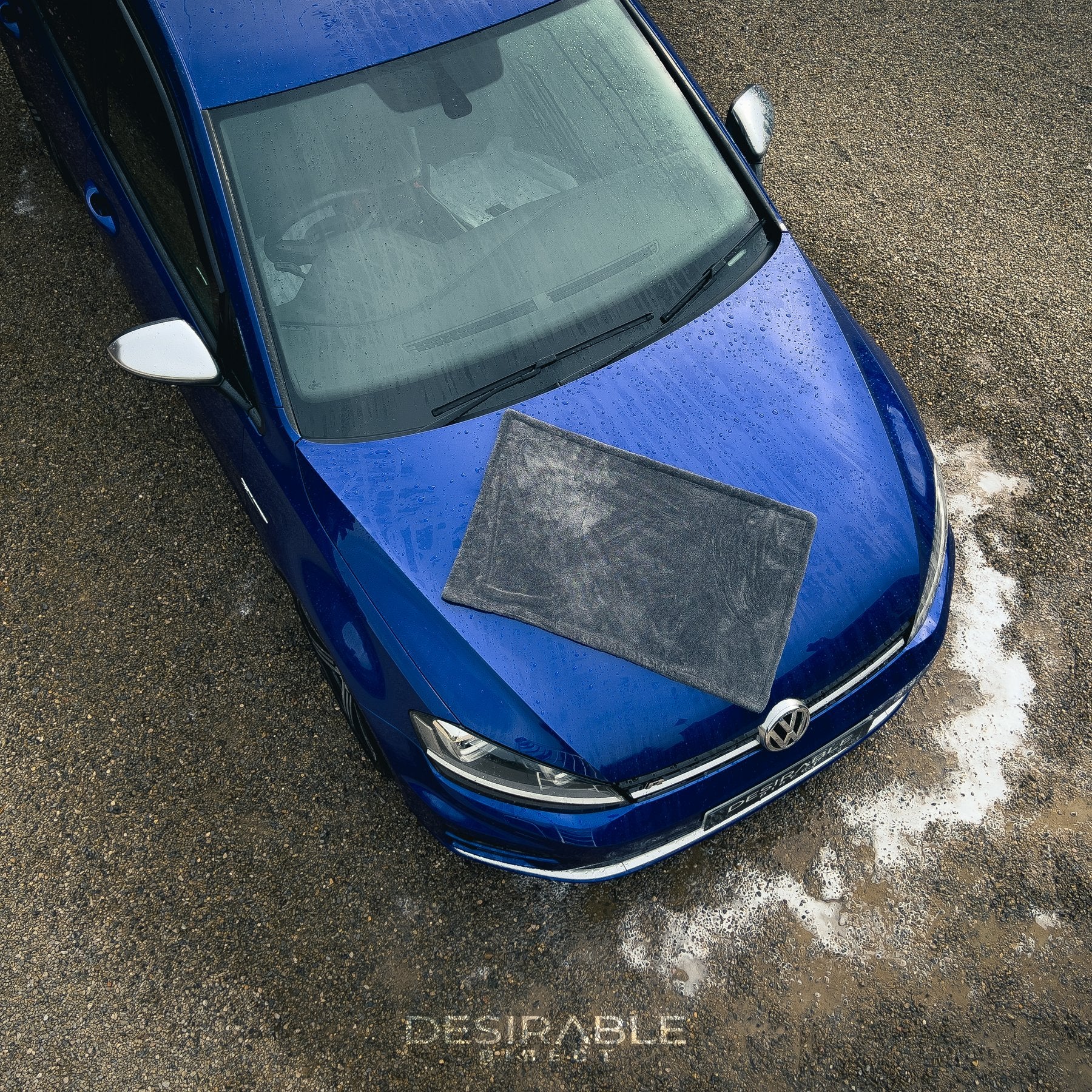Car care large twisted pile grey drying towel displayed on the bonnet of a blue volkswagen golf r. The vehicle is wet to showcase the drying capability of the towel and the photo is taken from an aerial view to show the size of the towel.