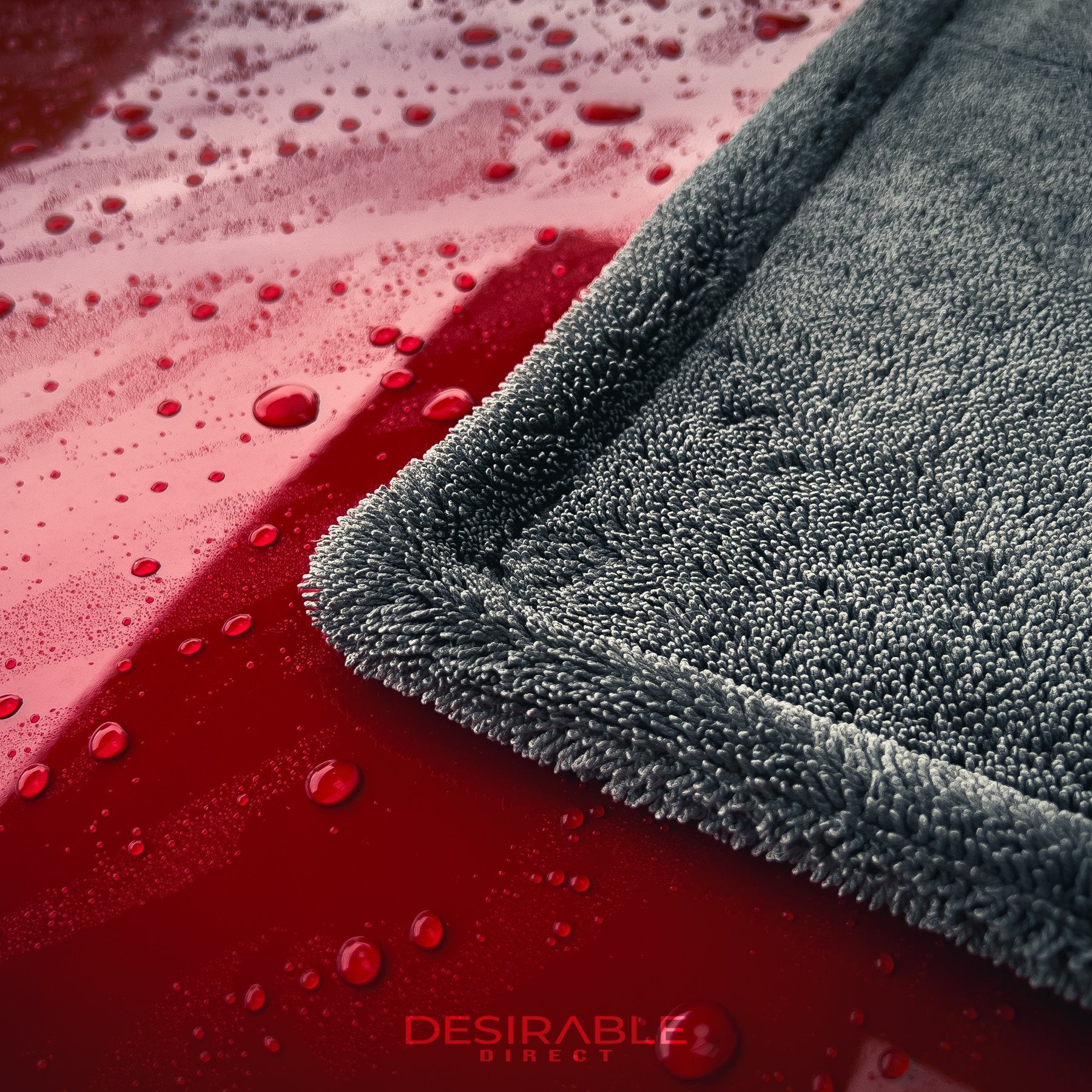 Car care large twisted pile grey drying towel showcased on the roof of a red car covered in water. This is a close up photo of the towel to show the water on the roof and the towel.