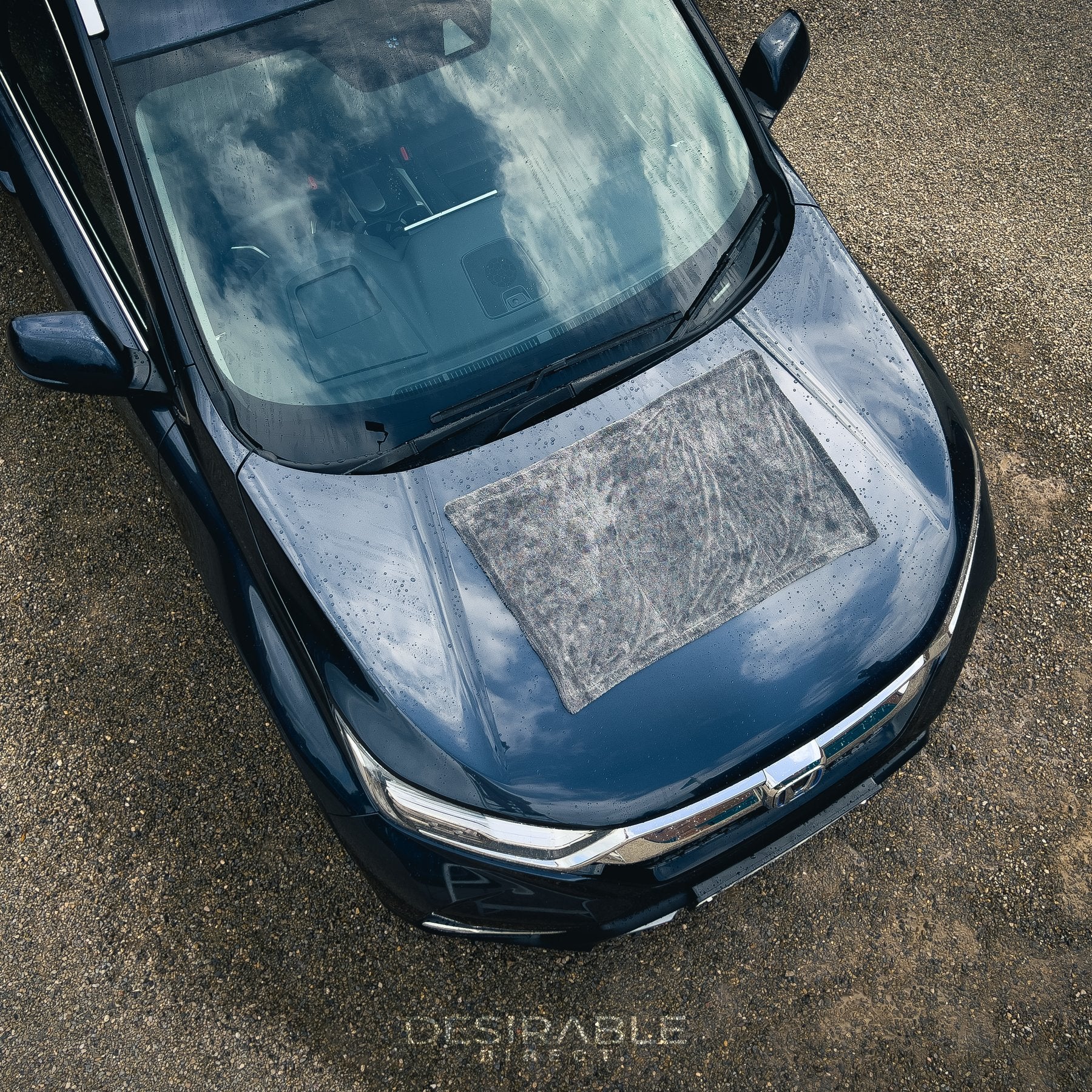 Car care large twisted pile grey drying towel displayed on the bonnet of a grey car. The vehicle is wet to showcase the drying capability of the towel. The photo was taken from an aerial view to showcase the size of the towel.
