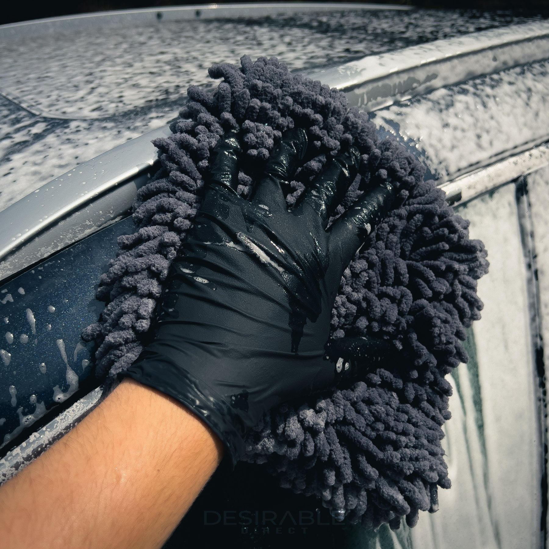 Car care large grey noodle wash pad. The wash pad is covered in car shampoo, with a hand wearing a black glove moving the pad across the paintwork of a grey car while completing the cleaning process.