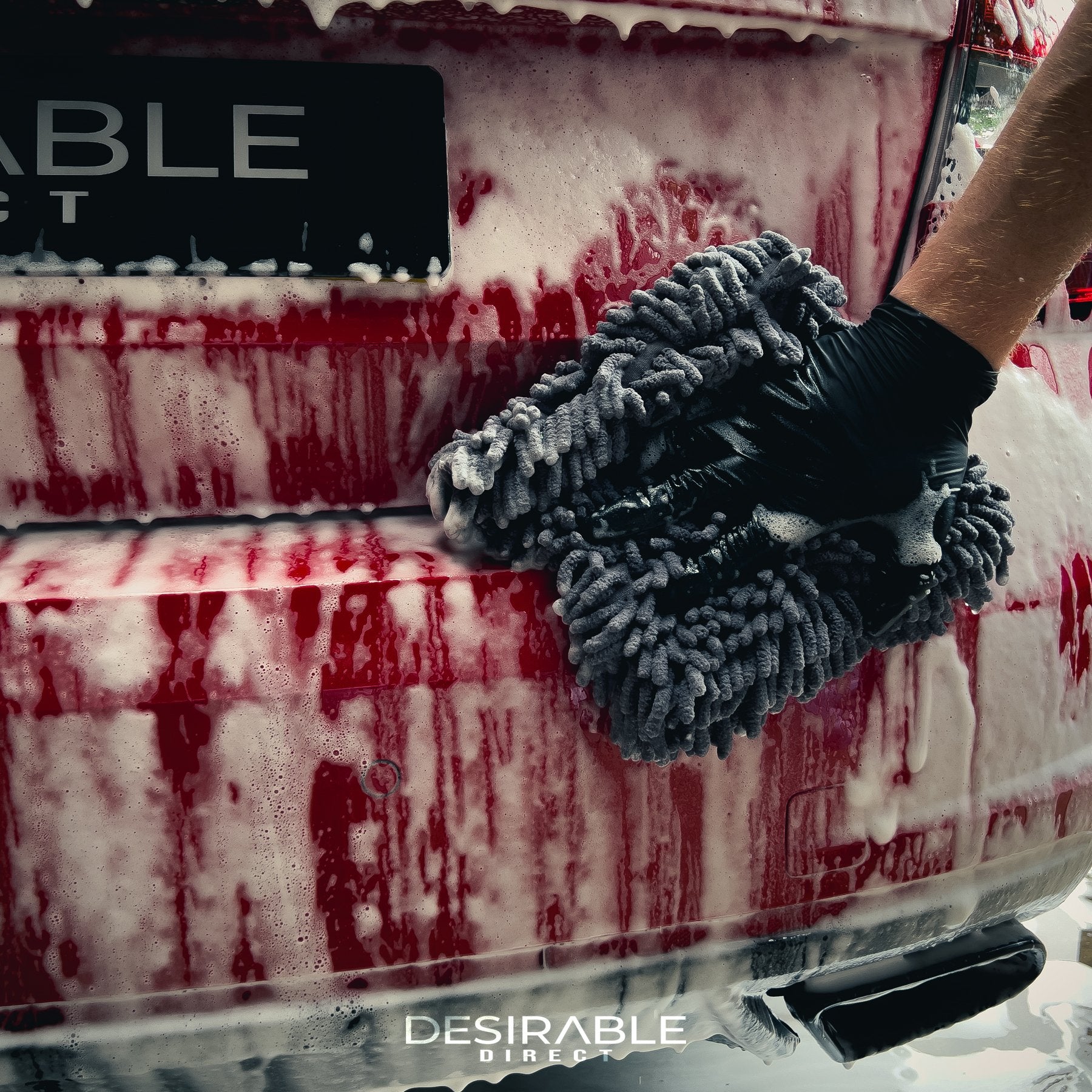 Car care large grey noodle wash pad. The wash pad is covered in car shampoo, with a hand wearing a black glove moving the pad across the paintwork of a red car while completing the cleaning process.
