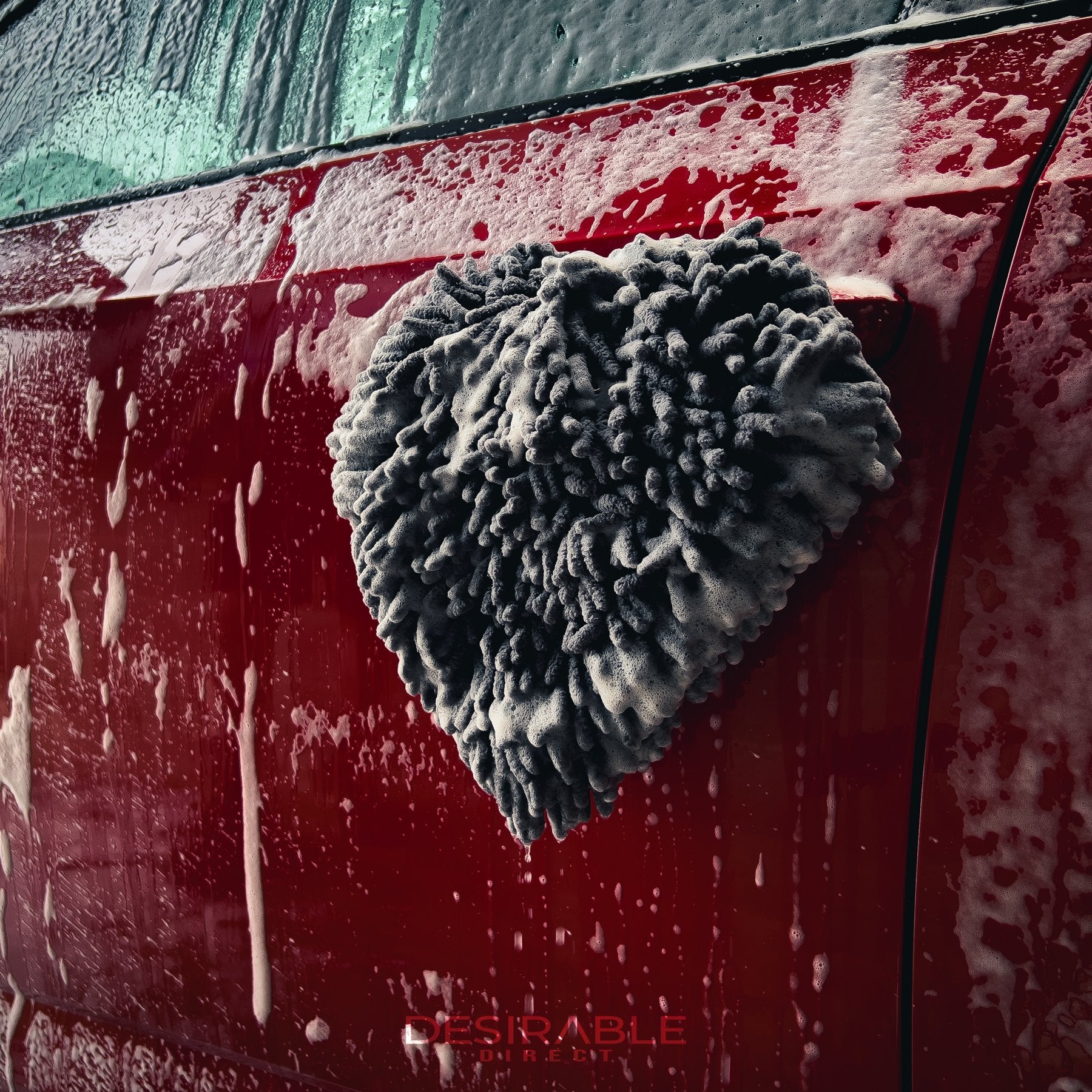 Car care large grey noodle wash pad. The wash pad is covered in car shampoo, hanging from the front passenger side door handle of a red car also covered in car shampoo.