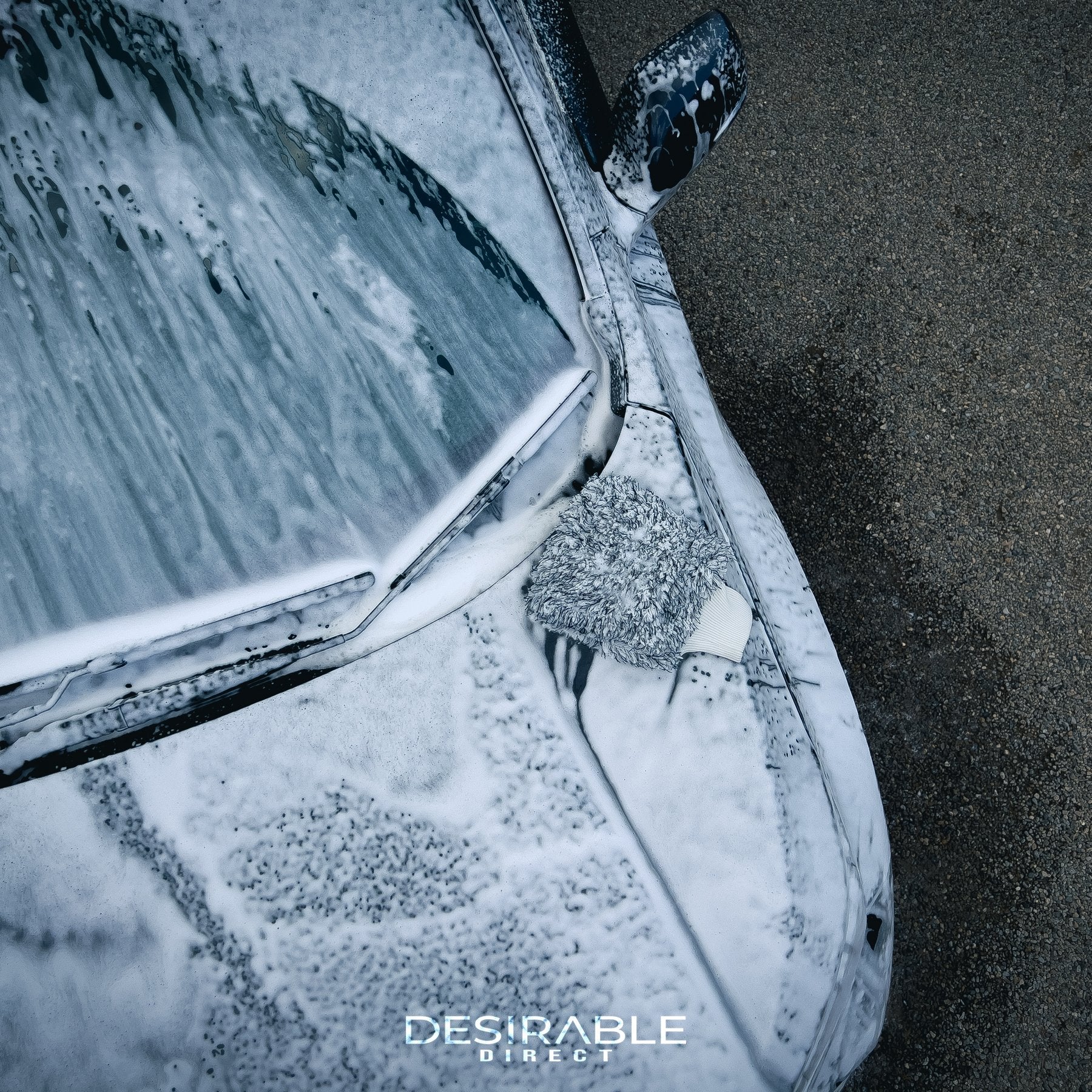 Car care microfibre black and white cleaning wash mitt displayed on the bonnet of a grey car covered in car shampoo. The photo is taken from an aerial view to show the cleaning mitt.
