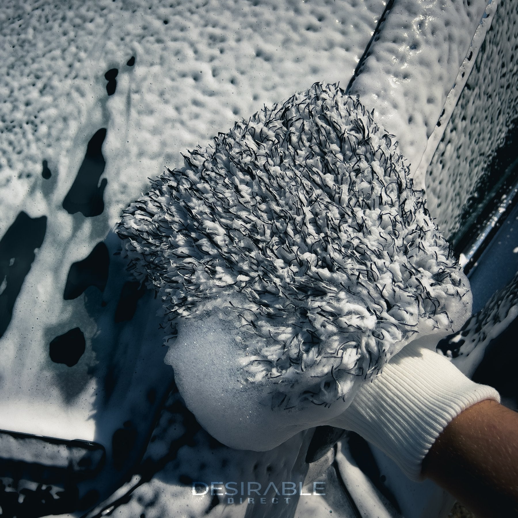 Car care microfibre black and white cleaning wash mitt cleaning a car covered in car shampoo. Somebody is holding the mitt while cleaning the car.