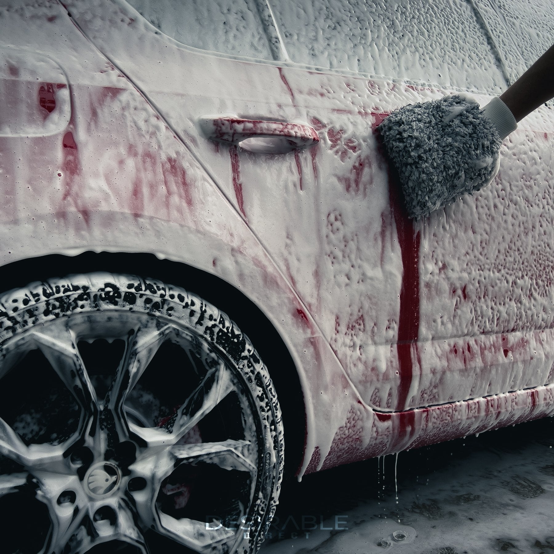 Car care microfibre black and white cleaning wash mitt cleaning a red car with black wheels covered in car shampoo. Somebody is holding the mitt while cleaning the car.