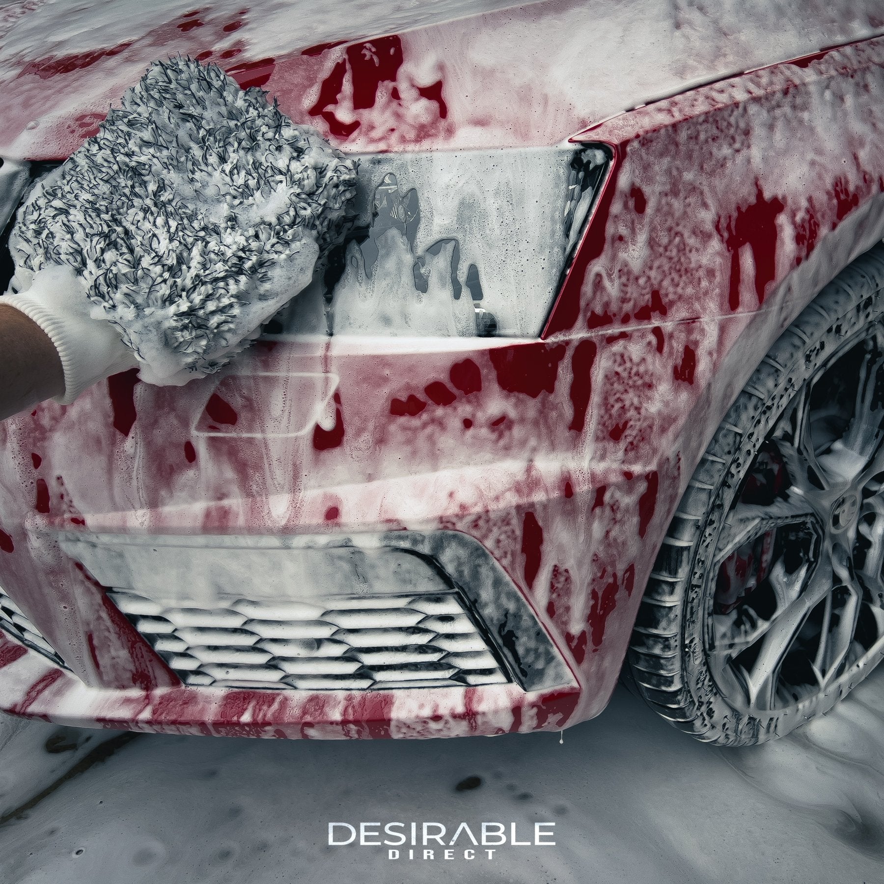 Car care microfibre black and white cleaning wash mitt cleaning the front bumper of a red car covered in car shampoo. Somebody is holding the mitt while cleaning the car.