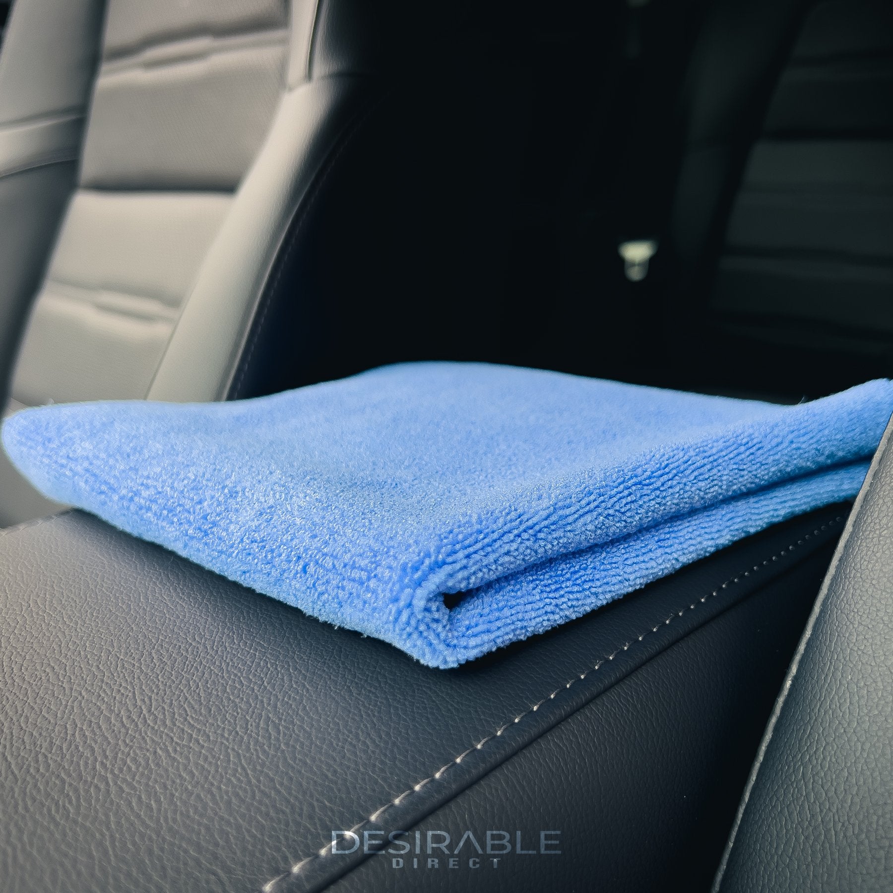 Car care microfibre soft blue multi-purpose cloth 40x40cm folded on a leather armrest in the centre of a car.