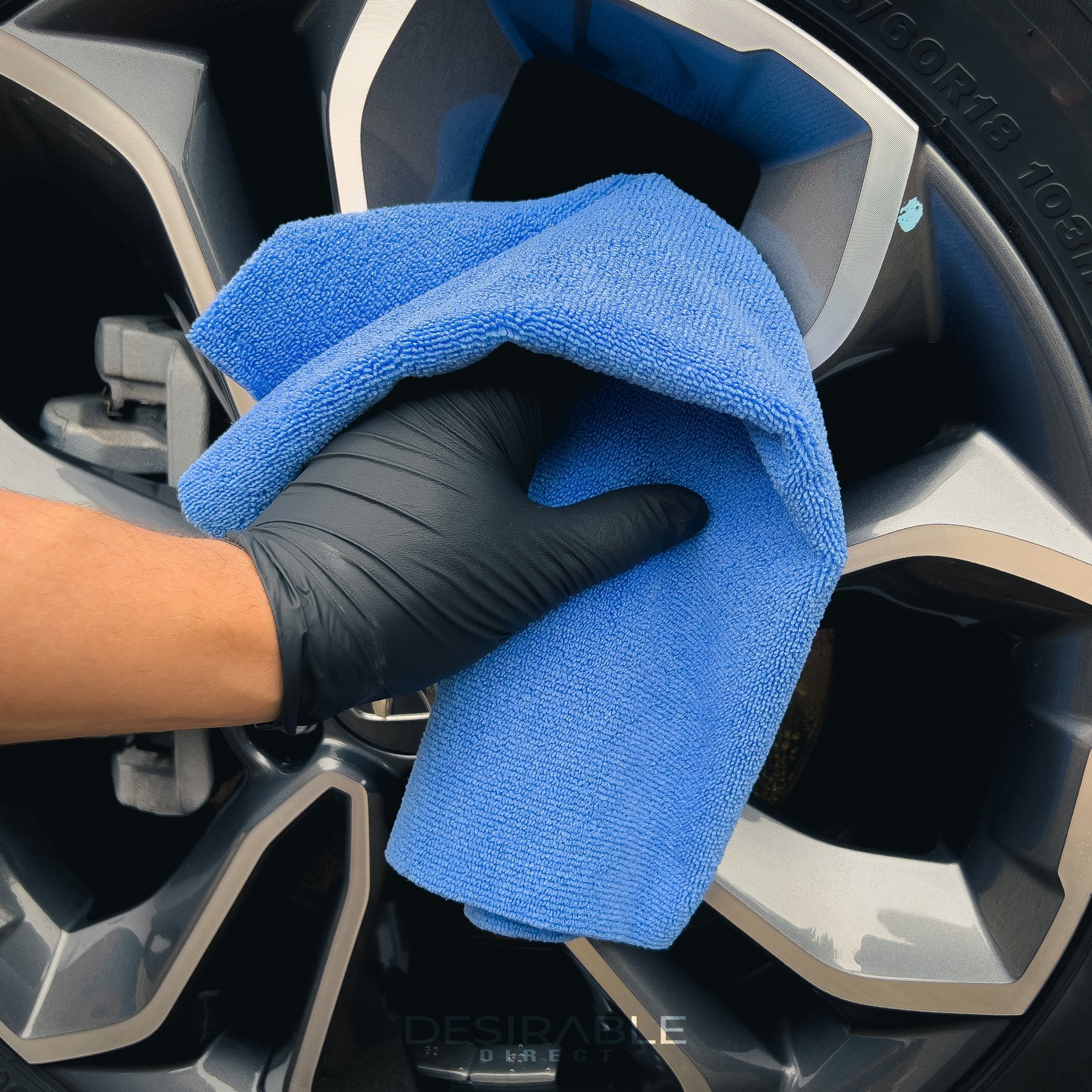 Car care microfibre soft blue multi-purpose cloth 40x40cm cleaning silver alloys of a grey car. The person holding the cloth is wearing black gloves.