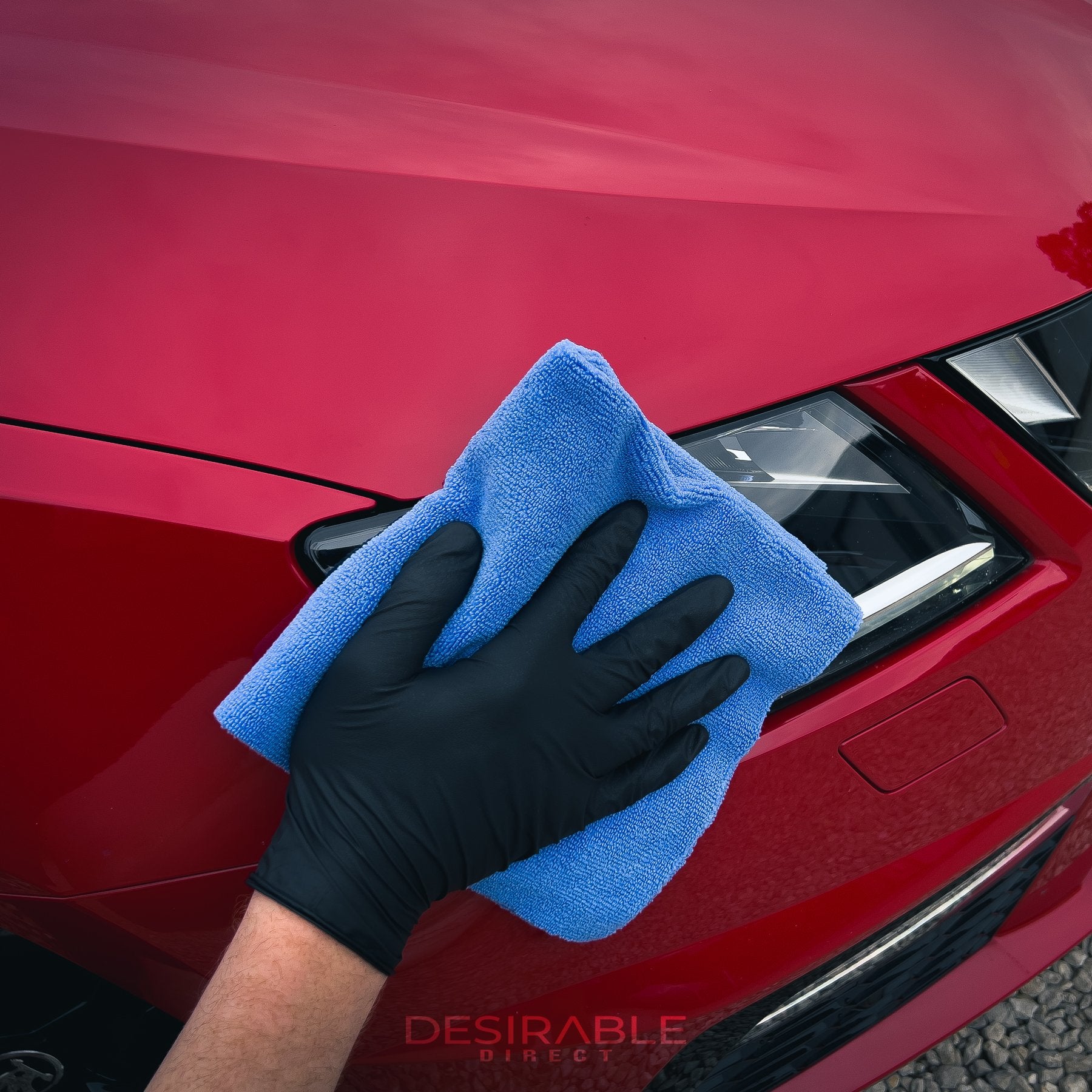 Car care microfibre soft blue multi-purpose cloth 40x40cm cleaning the front of a red car. The person holding the cloth is wearing black gloves.