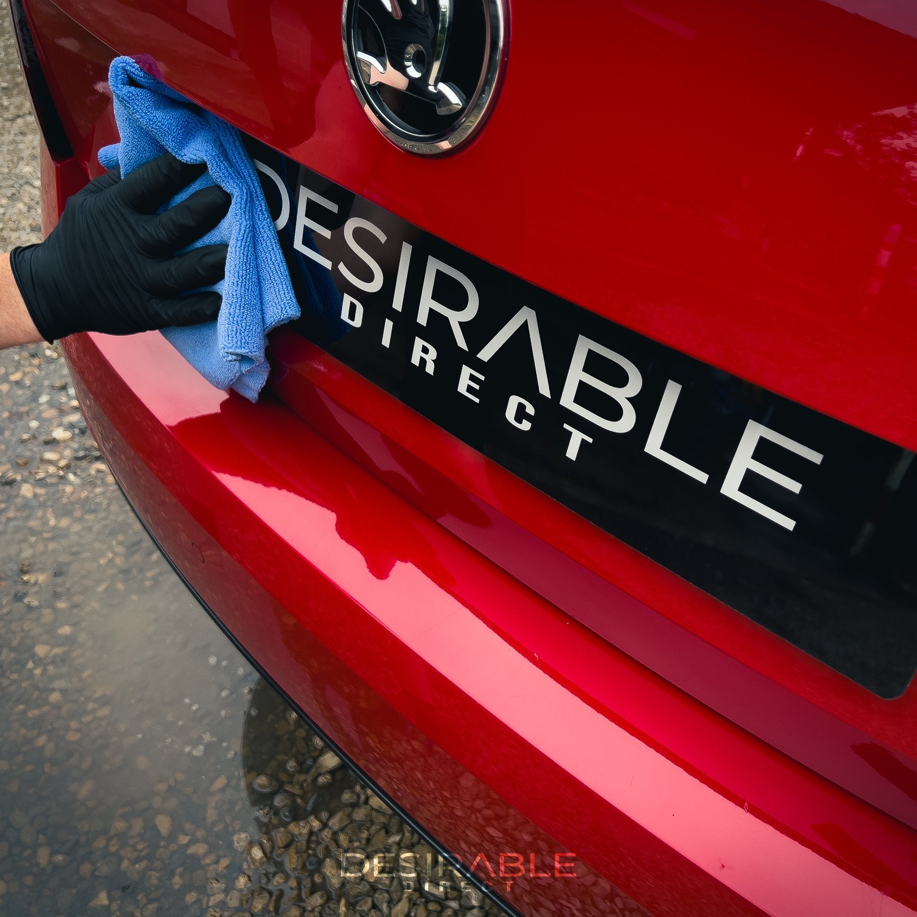 Car care microfibre soft blue multi-purpose cloth 40x40cm cleaning the back of a red car. The person holding the cloth is wearing black gloves.
