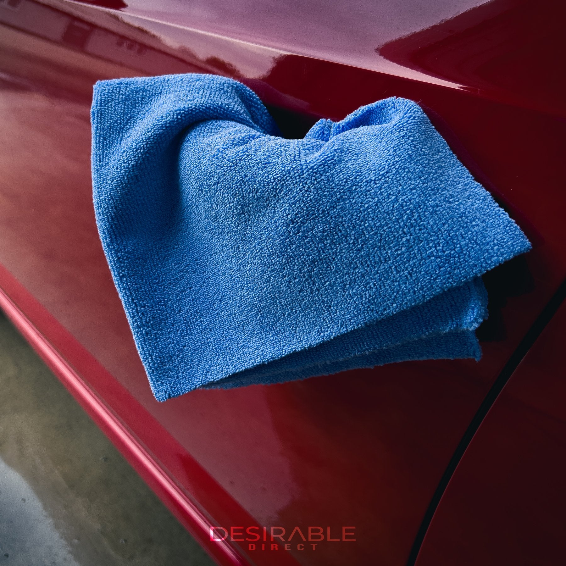 Car care microfibre soft blue multi-purpose cloth 40x40cm hanging from the passenger side door handle of a red car.