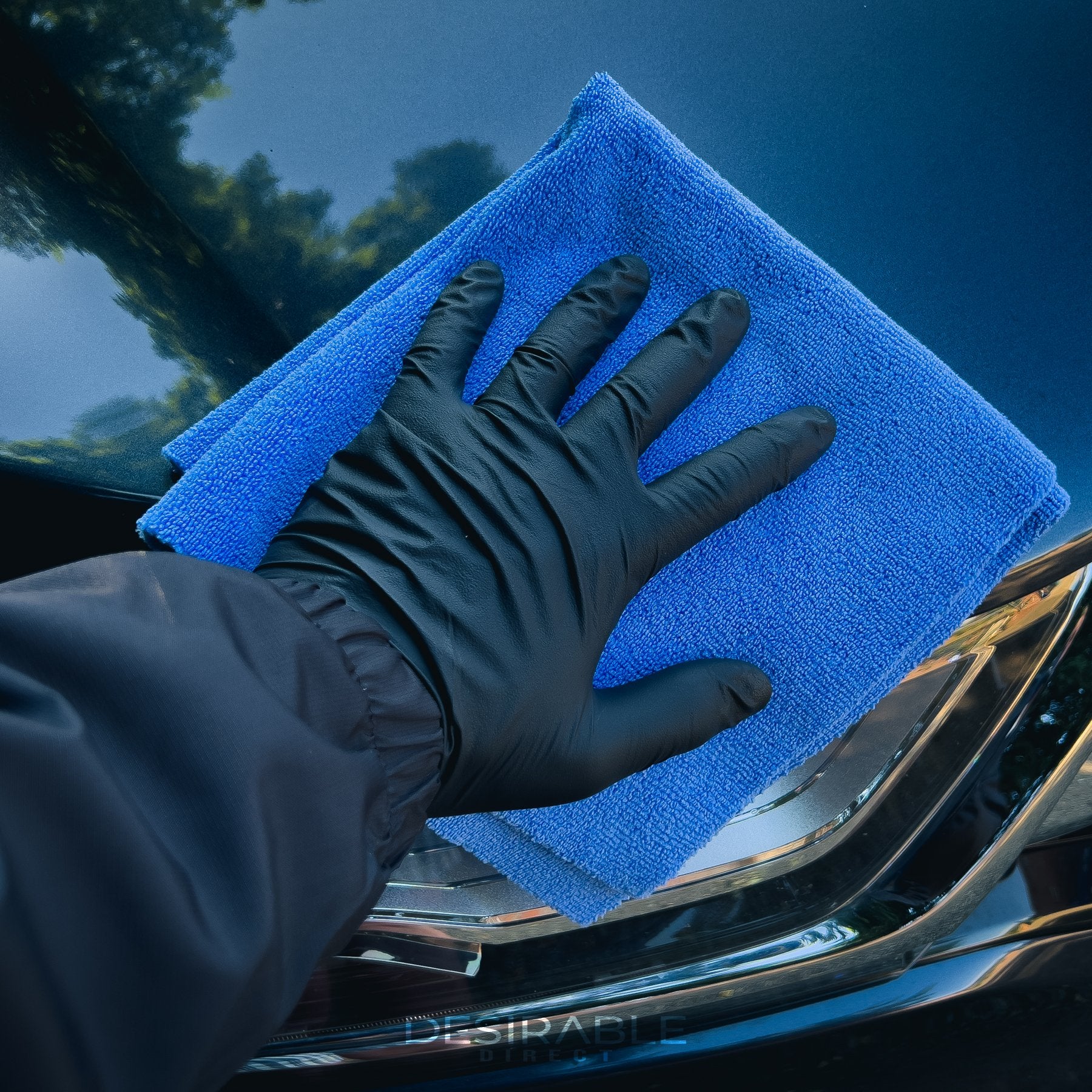 Car care microfibre soft blue multi-purpose cloth 40x40cm cleaning the front of a grey car. The person holding the cloth is wearing black gloves.