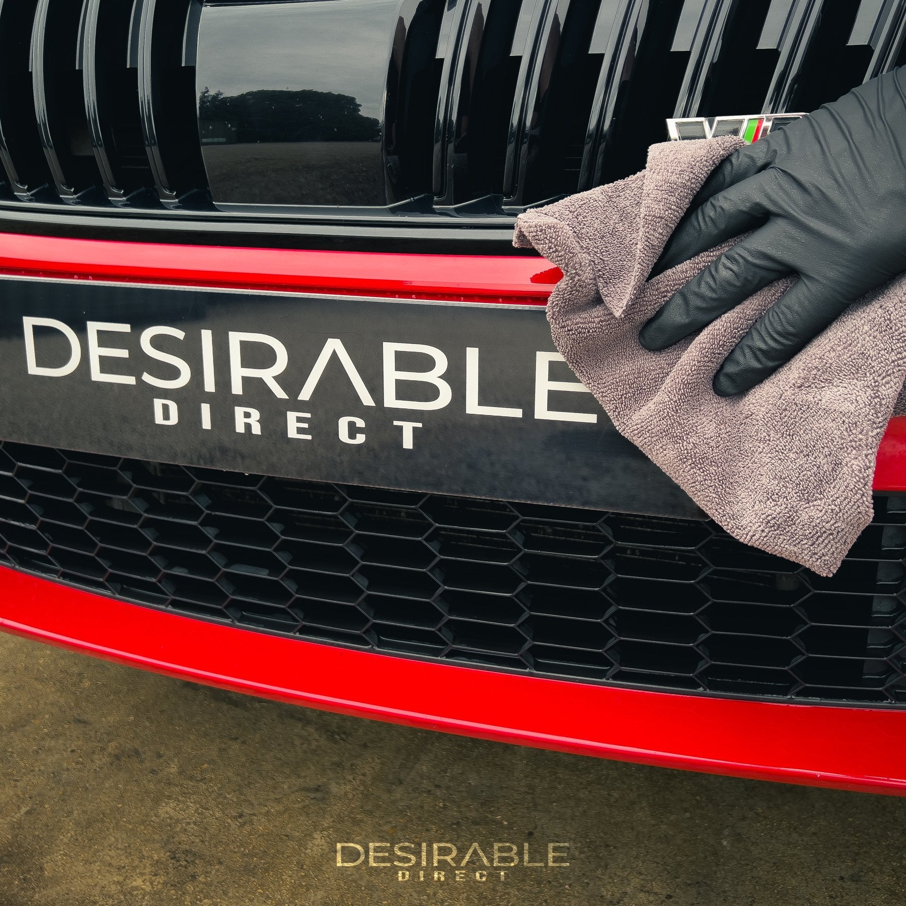 Car care microfibre grey cloth 40x40cm cleaning the front of a red car. The person holding the cloth is wearing black gloves.