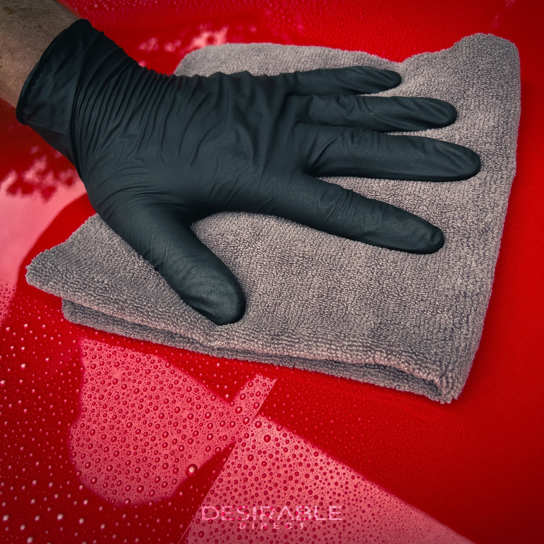Car care microfibre grey cloth 40x40cm cleaning the bonnet of a red car using car quick detailer. The person holding the cloth is wearing black gloves.