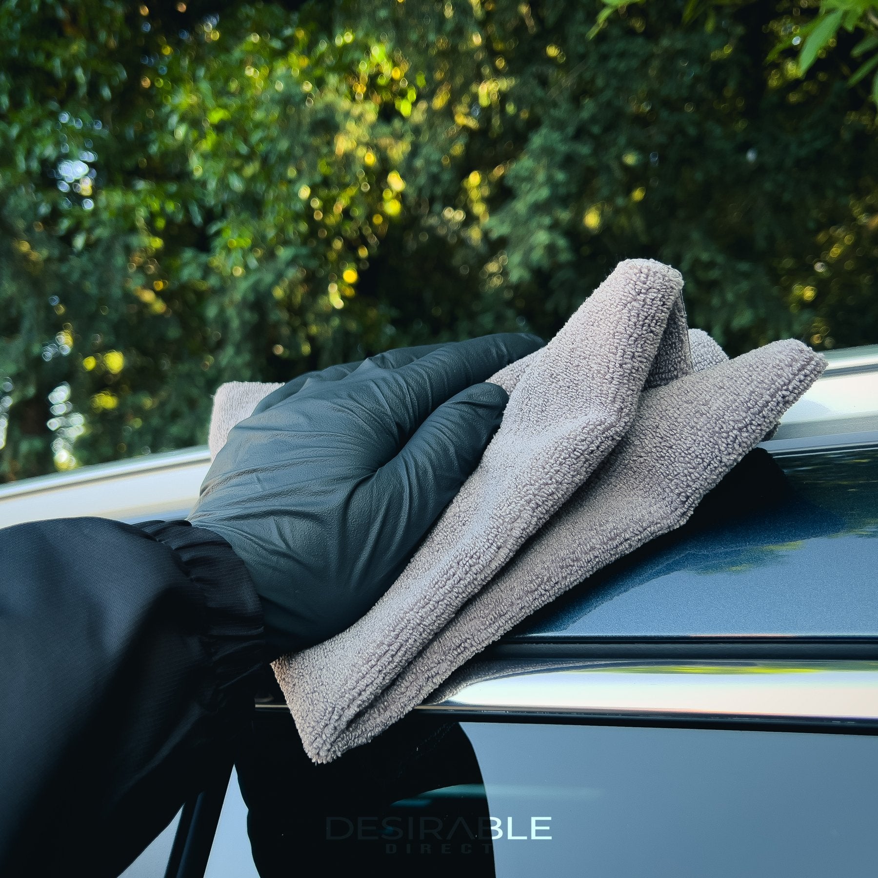 Car care microfibre grey cloth 40x40cm cleaning the roof of a grey car. With green leaves in the background.