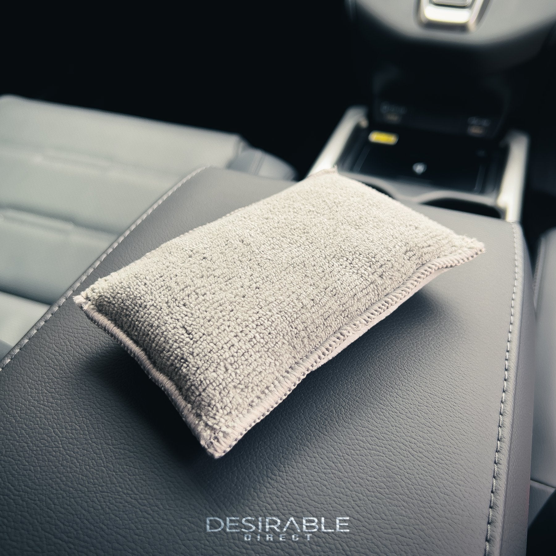 Car care one microfibre grey interior scrub pad showcased on a leather armrest in the centre of a car.