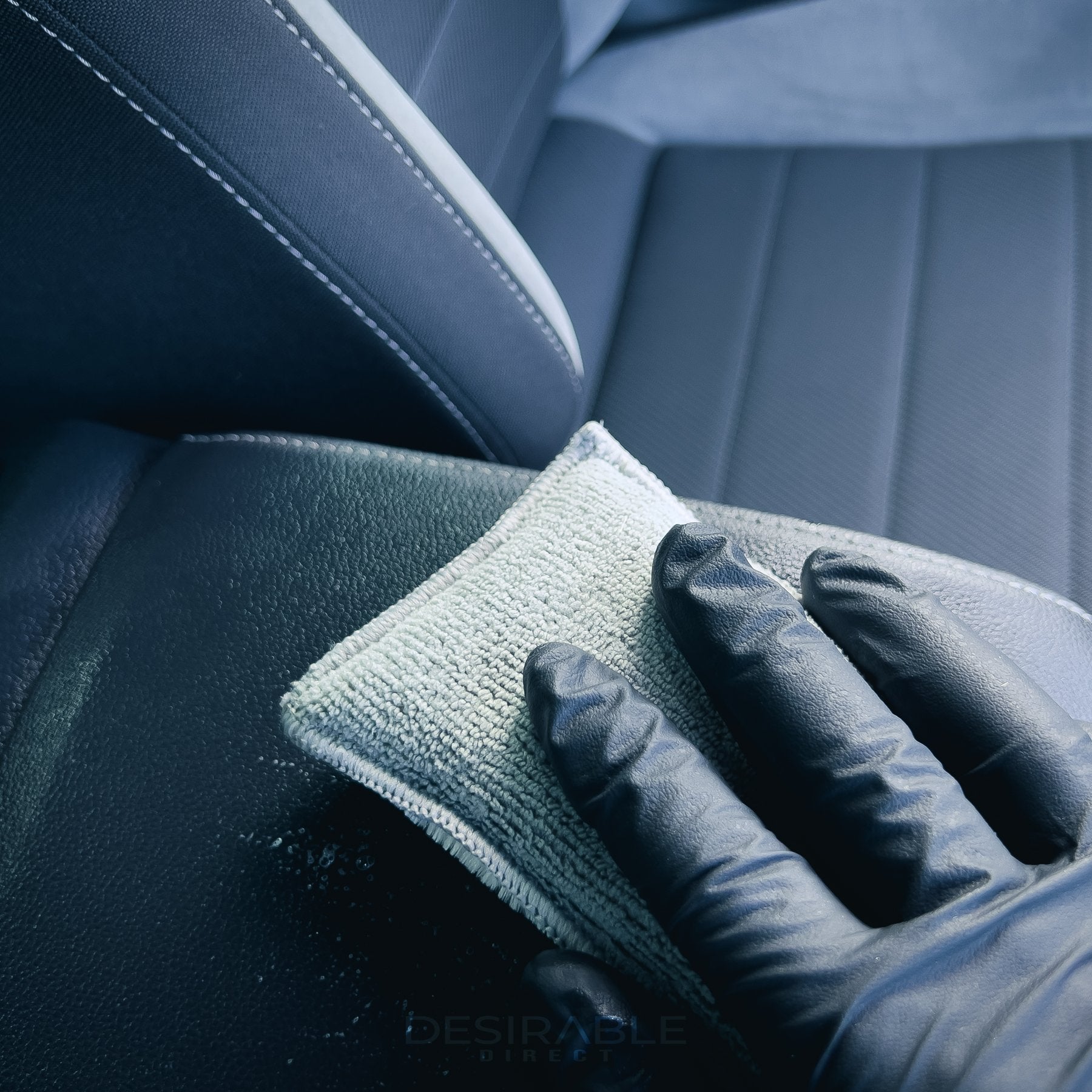 Car care one microfibre grey interior scrub pad cleaning a leather armrest in a volkswagen golf r. Somebody is holding the pad while wearing black gloves.