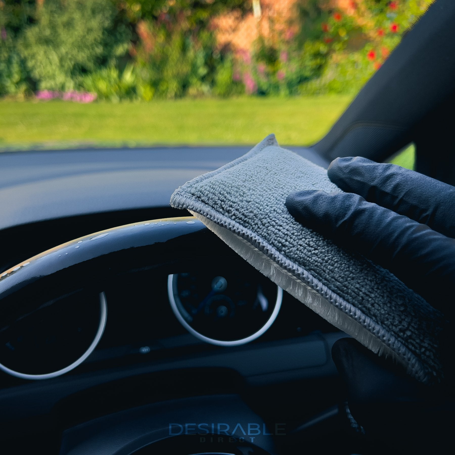Car care one microfibre grey interior scrub pad cleaning the top of the steering wheel of a volkswagen golf r. Somebody is holding the pad while wearing black gloves.