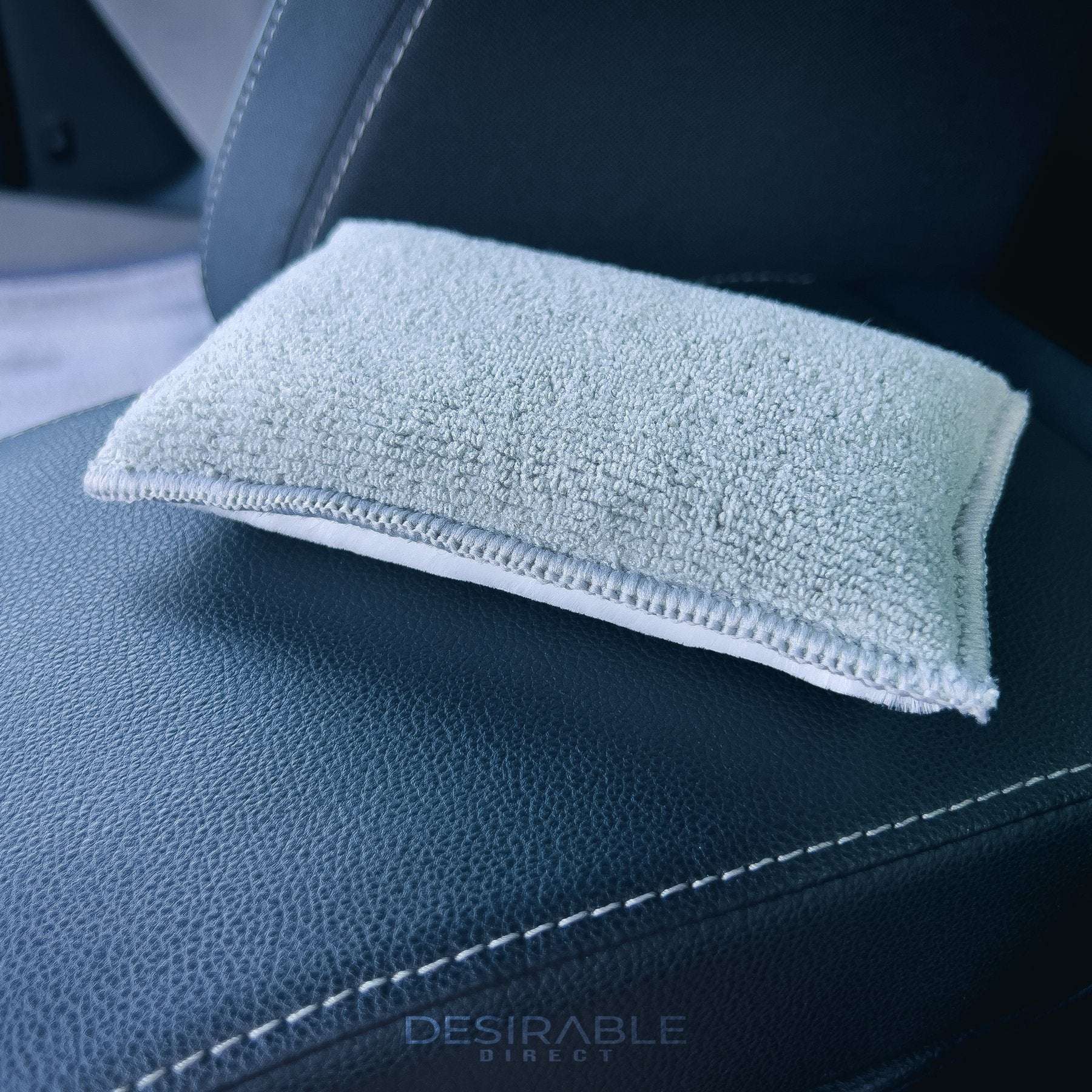 Car care one microfibre grey interior scrub pad is showcased on a leather armrest in the centre of a car. This is a close-up photo to show the scrub pad.