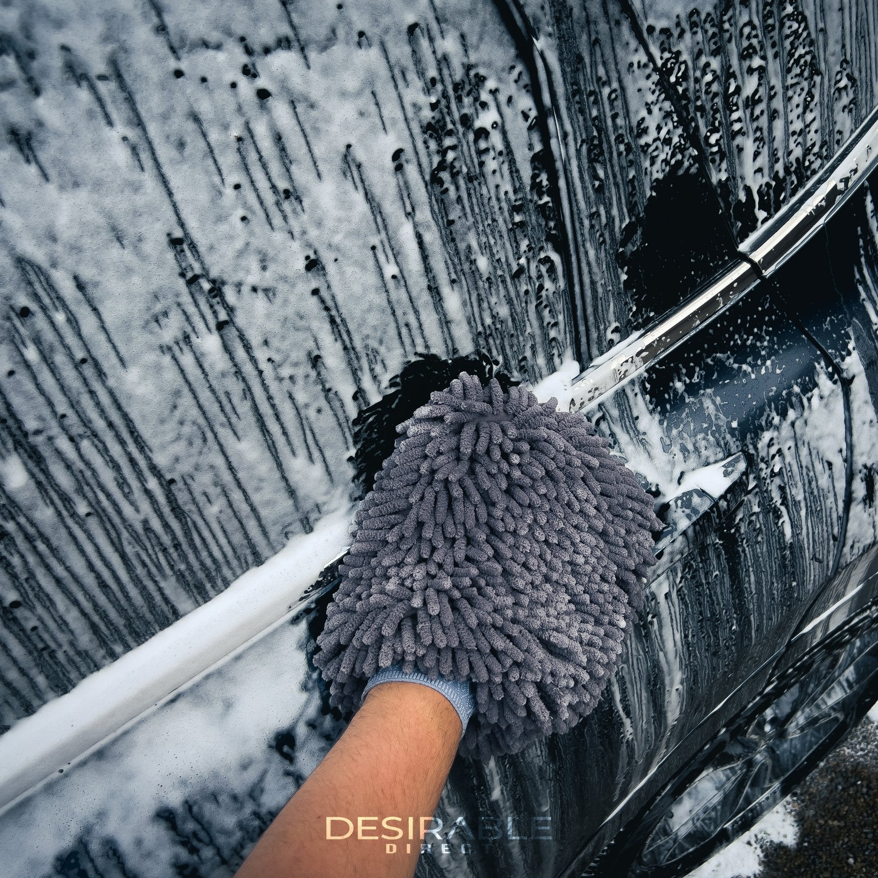 Car care noodle chenille grey wash mitt cleaning the side of a grey car covered in car shampoo.