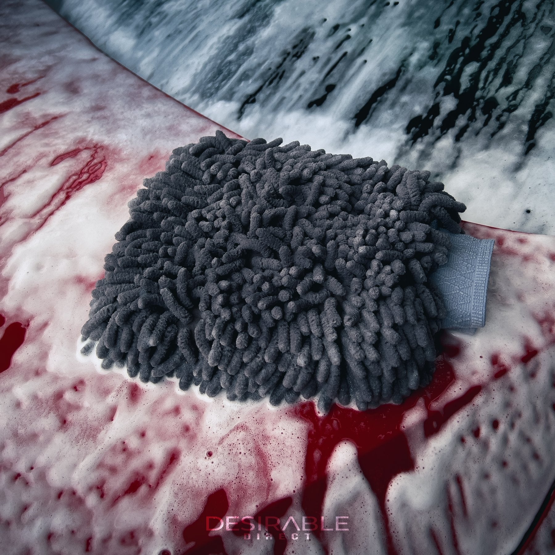 Car care noodle chenille grey wash mitt on the bonnet of a red car covered in car shampoo.