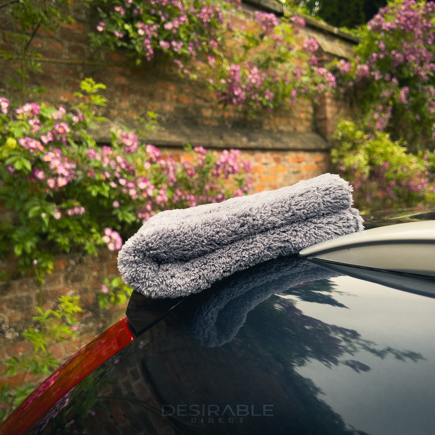 Car care plush grey microfibre cloth displayed on the roof of a grey car. With pink flowers in the background.