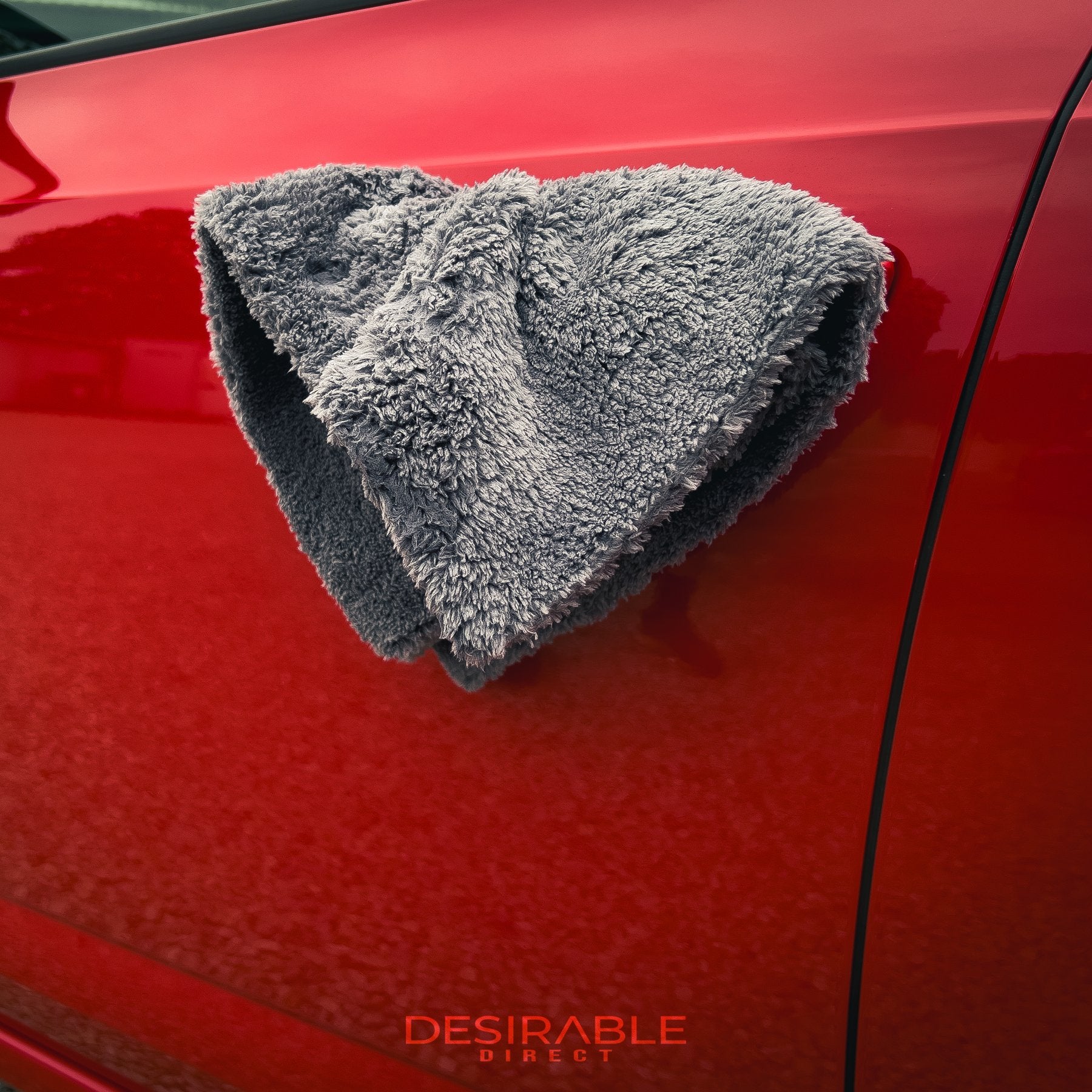 Car care plush grey microfibre cloth hanging from the passenger door handle of a red car.