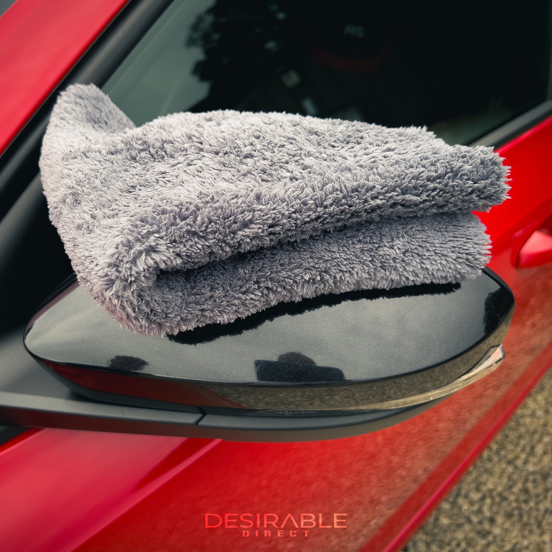 Car care plush grey microfibre cloth folded and displayed on the passenger side mirror of a red car.