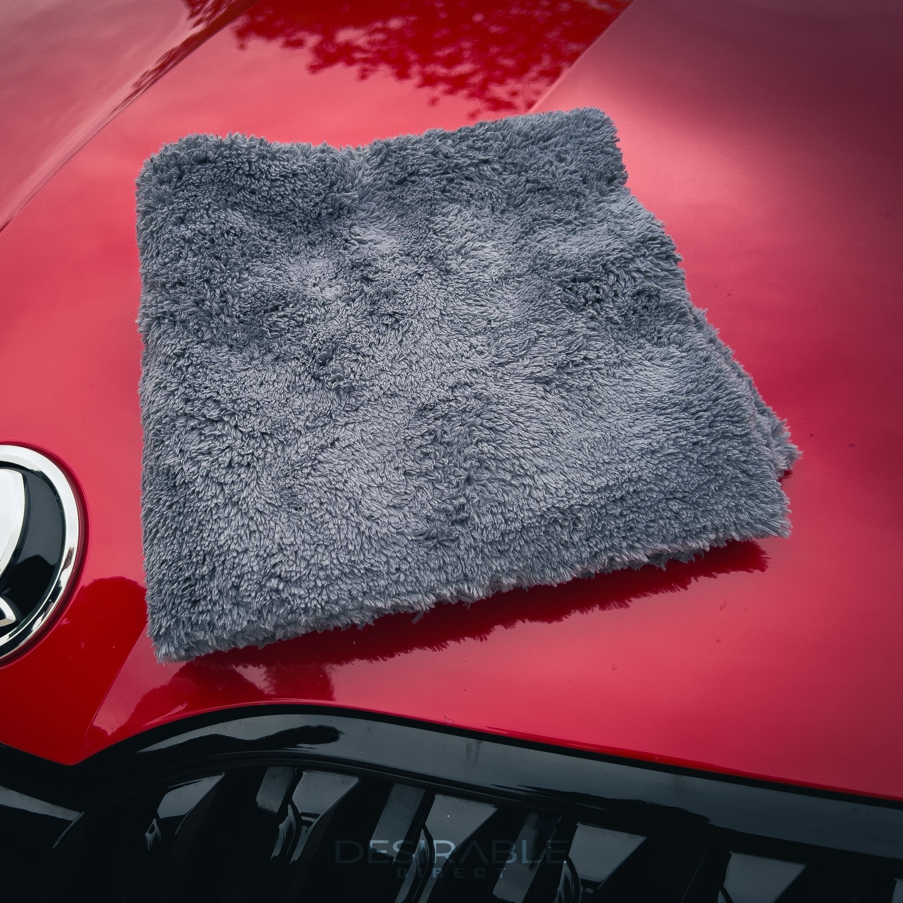 Car care plush grey microfibre cloth folded and displayed on the bonnet of a red car.