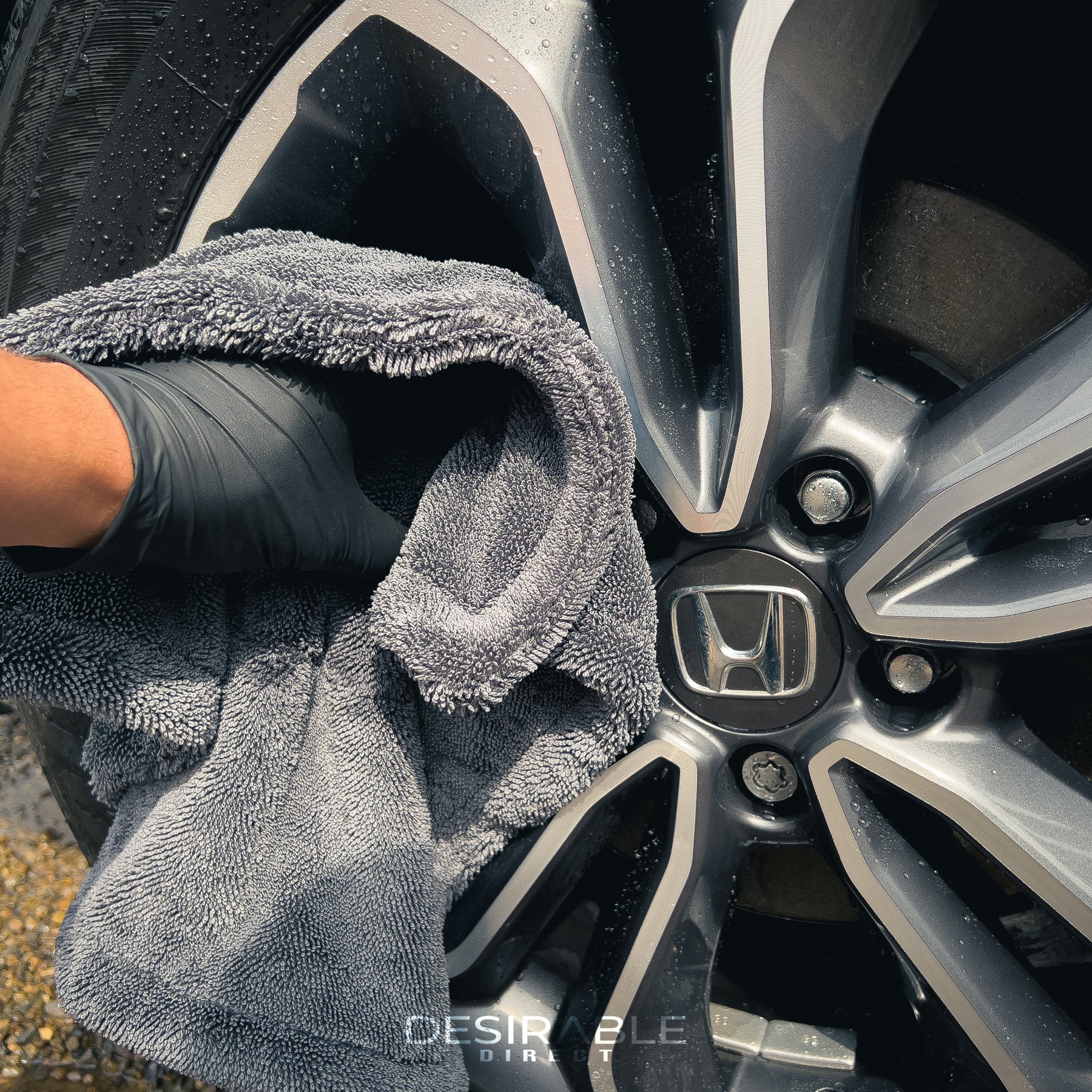Car care small twisted pile grey microfibre wheel and trim 40x40cm drying towel drying a silver alloy. The person holding the towel is wearing black gloves.