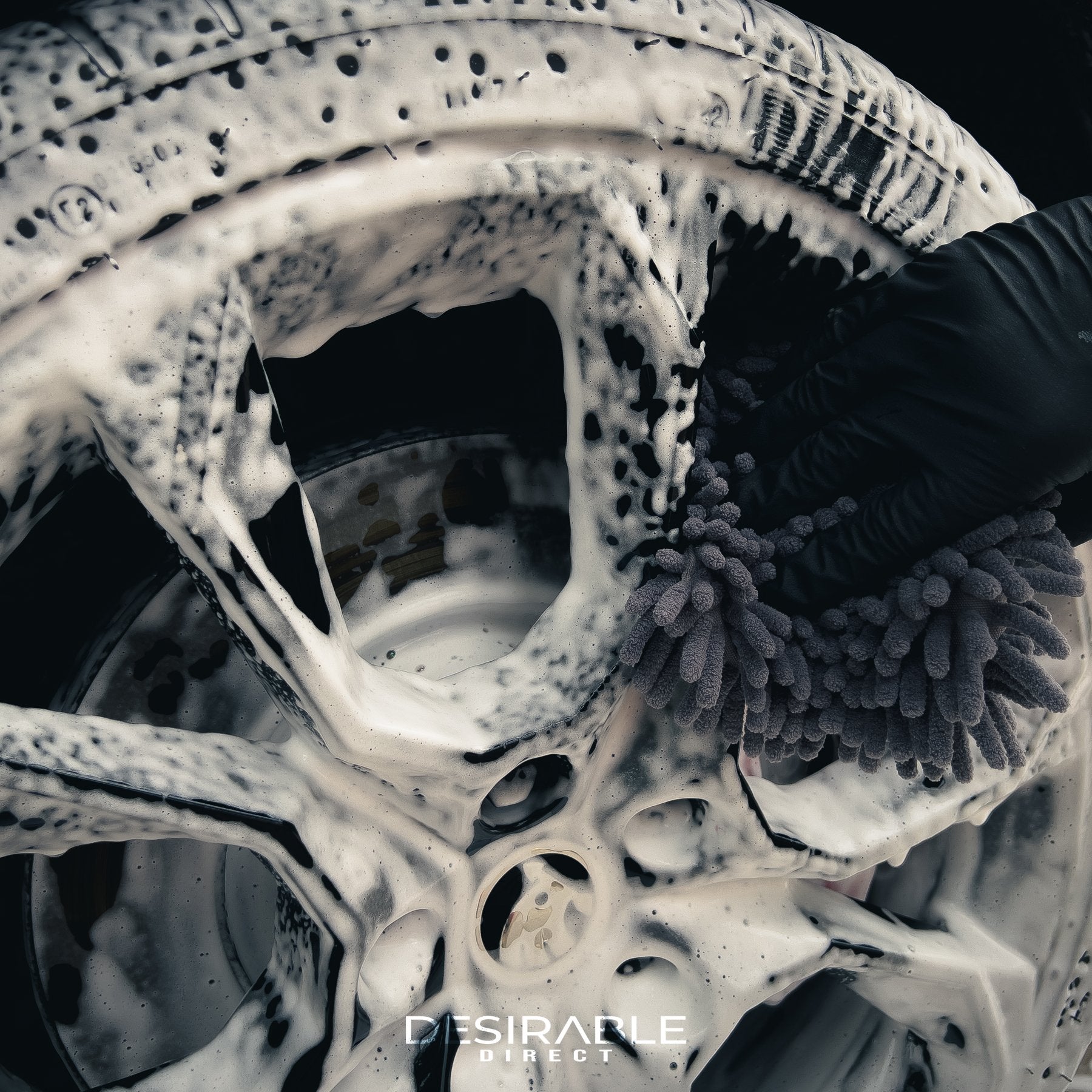 Car care chenille grey wheel and trim noodle wash pad cleaning black alloy wheels on a red car covered in car shampoo.