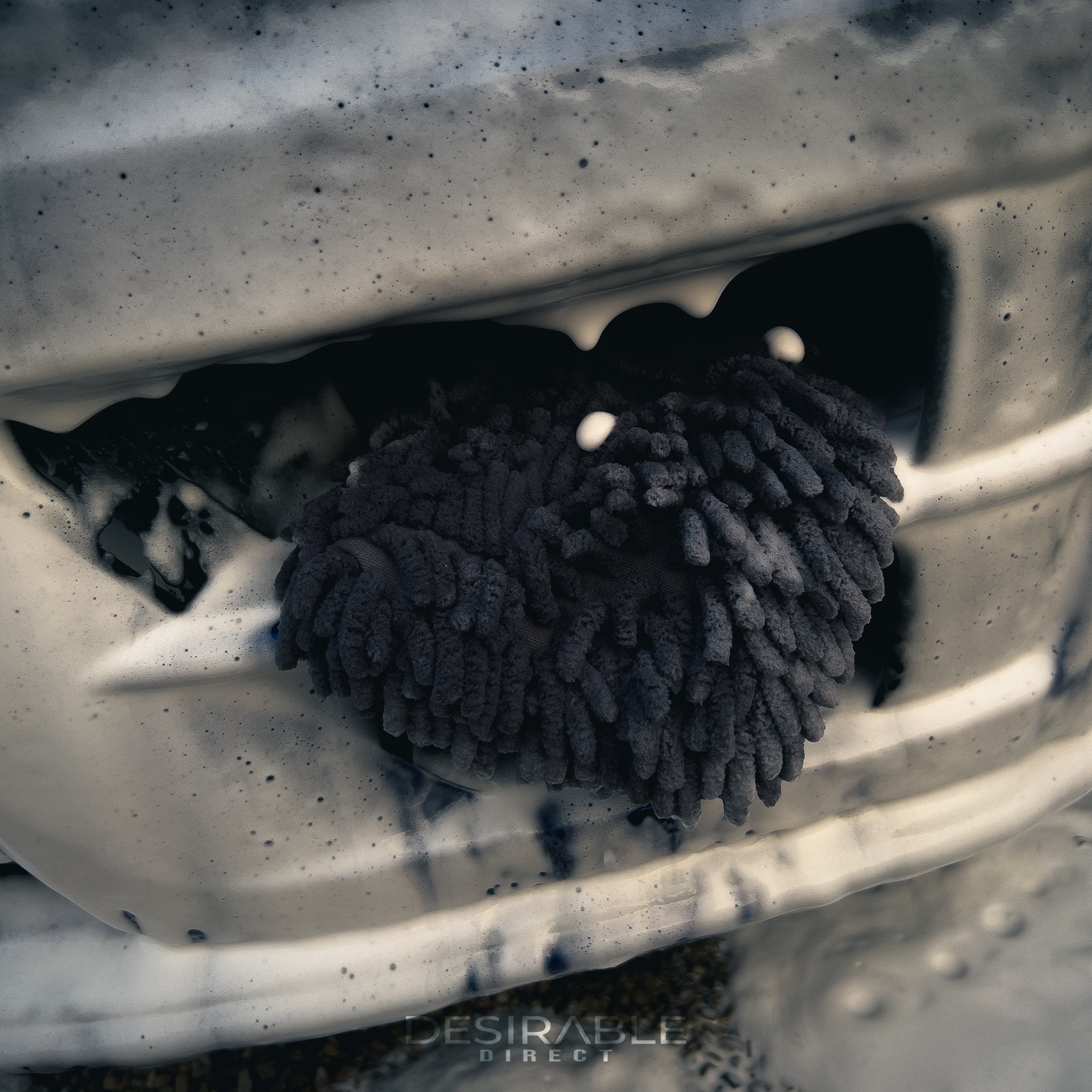 Car care chenille grey wheel and trim noodle wash pad displayed in the front grill of a blue volkswagen golf r covered in car shampoo.