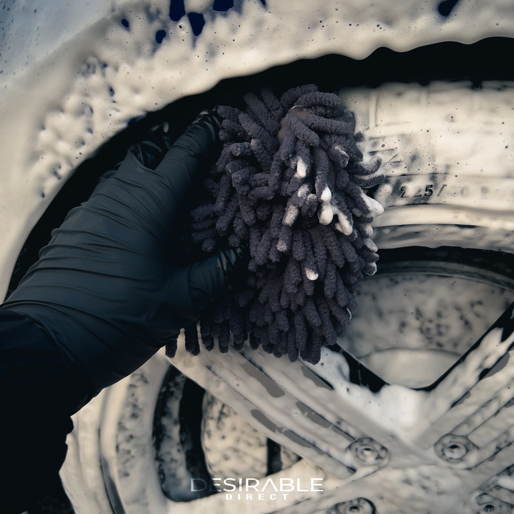 Car care chenille grey wheel and trim noodle wash pad cleaning the tyre of a blue volkswagen golf r covered in car shampoo.