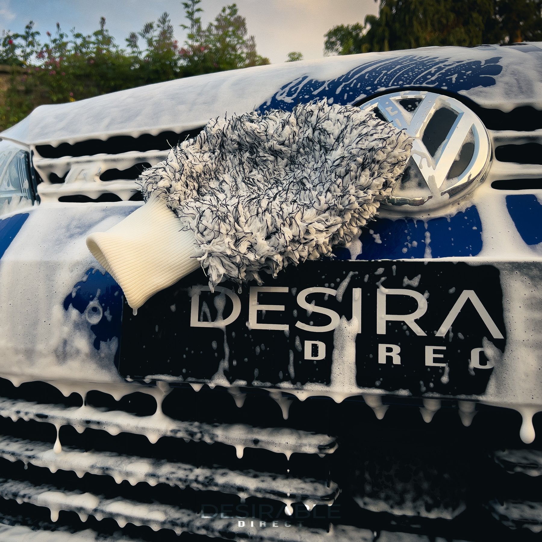 Car care microfibre black and white cleaning wash mitt hanging on the front bumper of a volkswagen golf r covered in car shampoo.