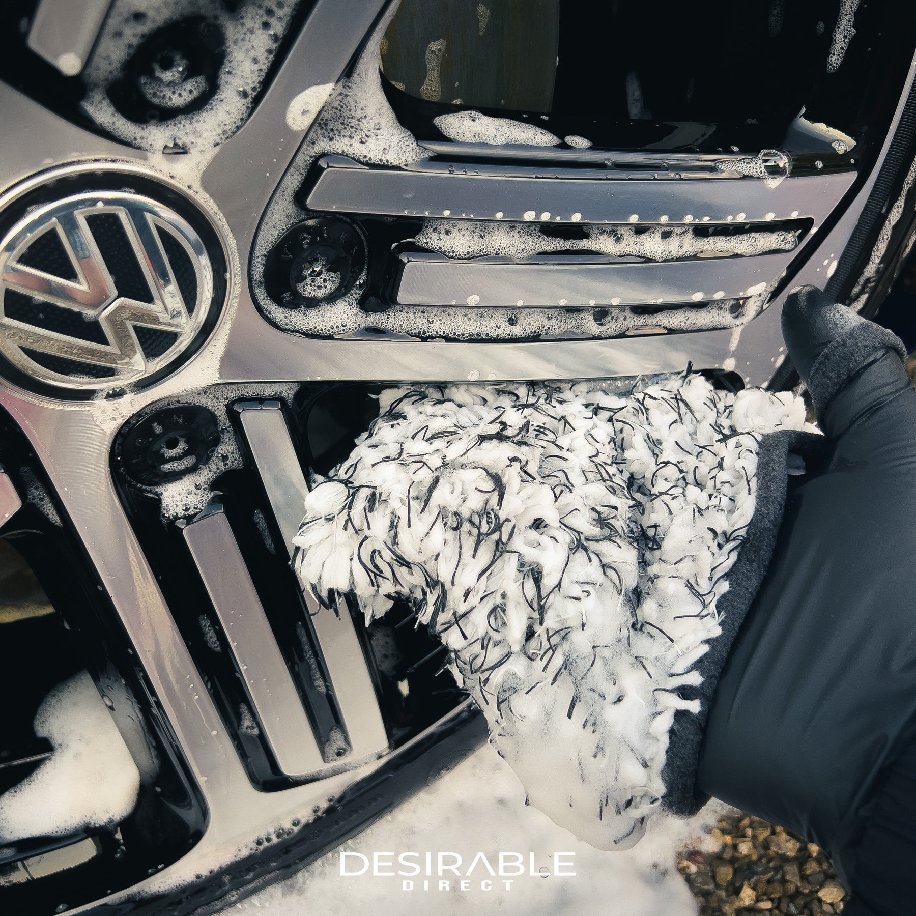 Car care microfibre wheel mitt cleaning the alloy wheel of a blue volkswagen golf r. The person holding the mitt is wearing a black glove.