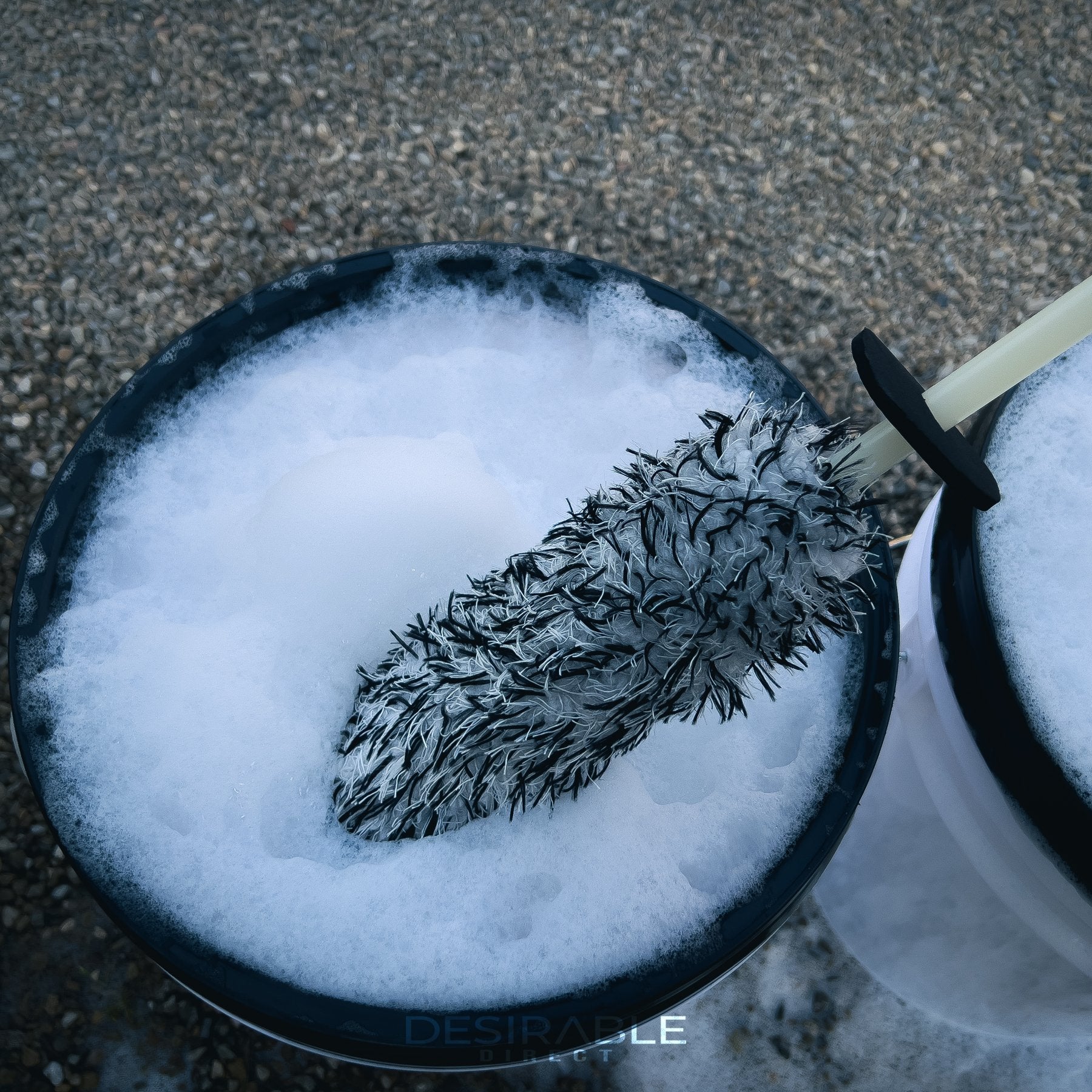 Car care microfibre black and white alloy wheel brush in a car cleaning bucket filled with water and car shampoo.