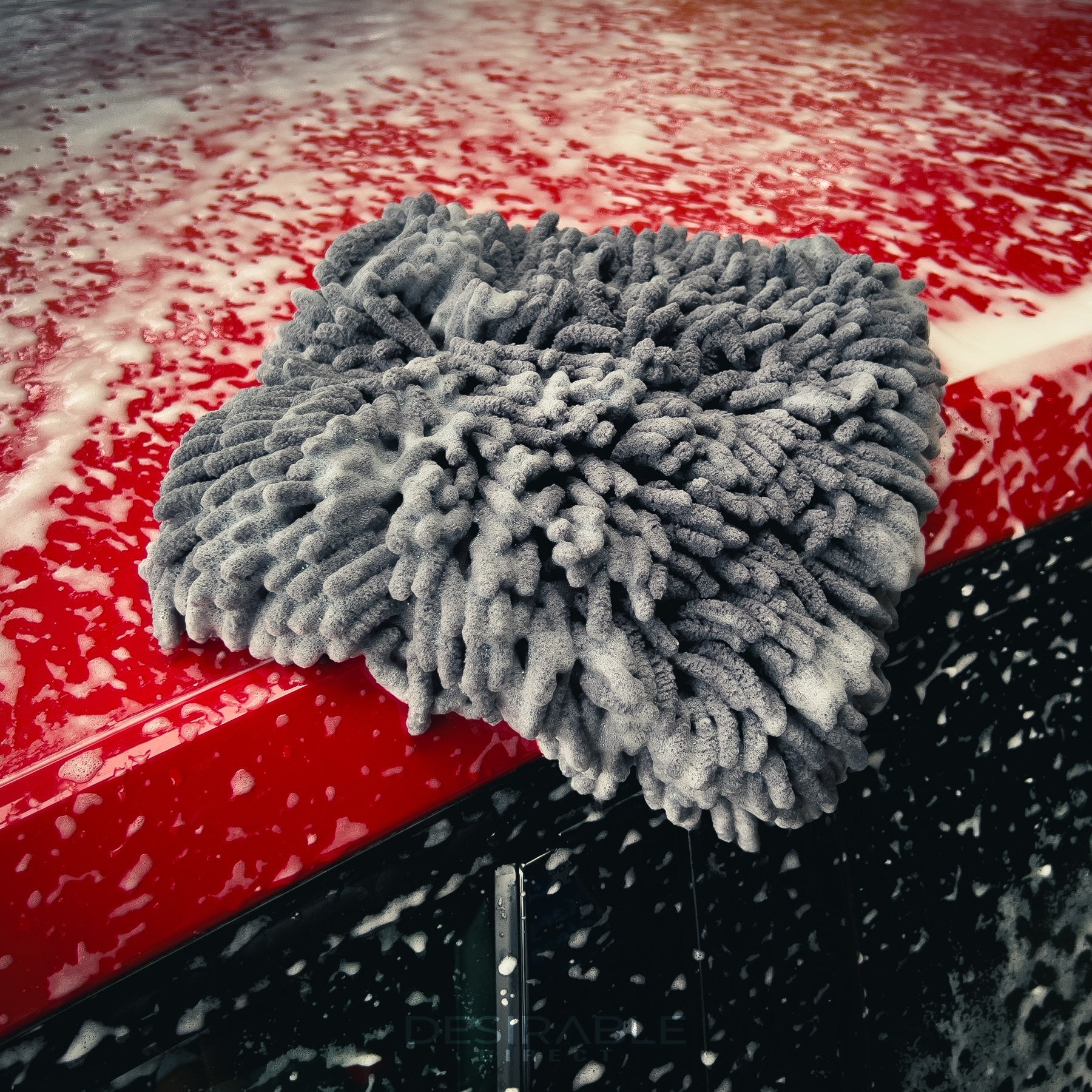 Car care noodle grey large pad on the roof of a red car covered in car shampoo.