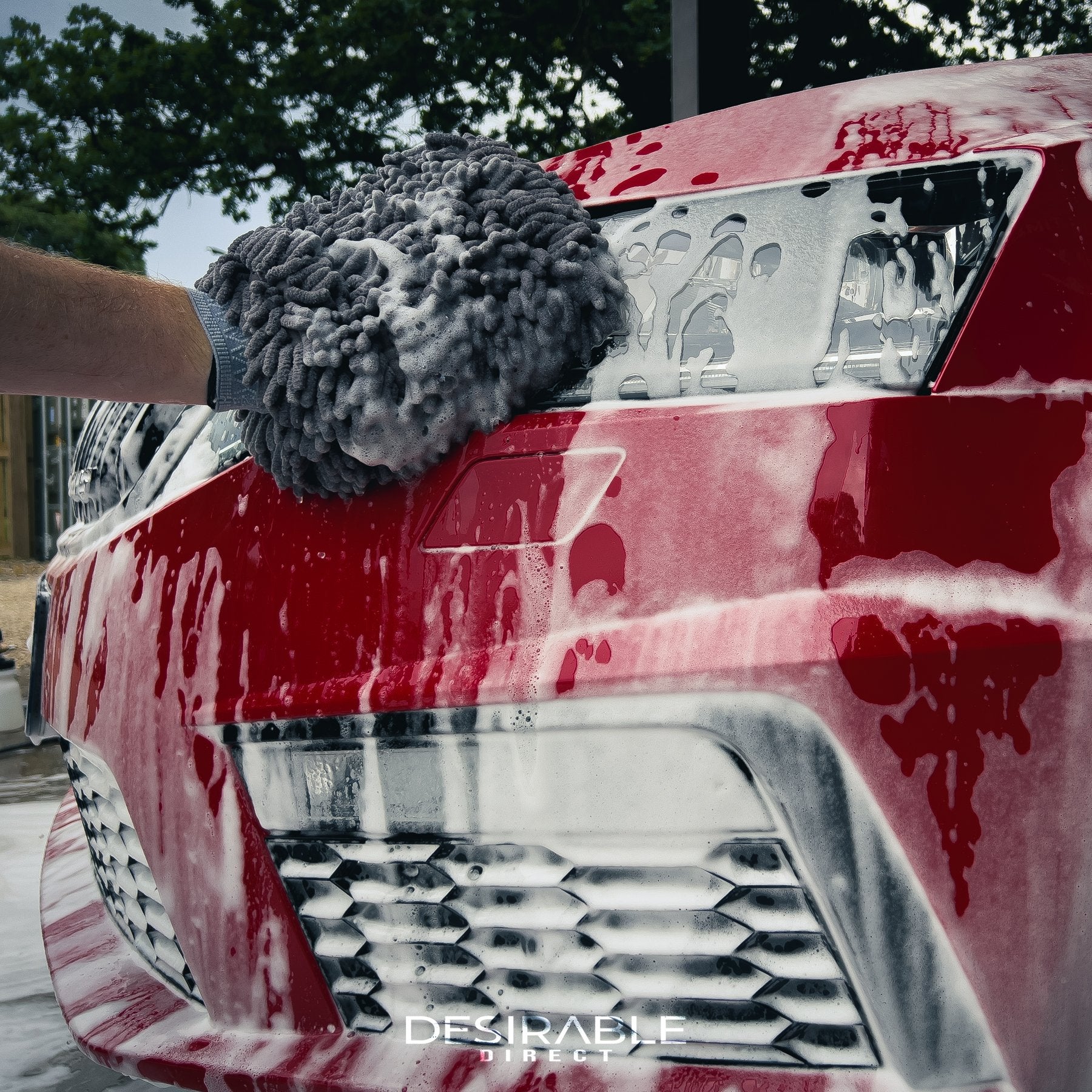 Car care noodle chenille grey wash mitt cleaning the front of a red car covered in car shampoo.