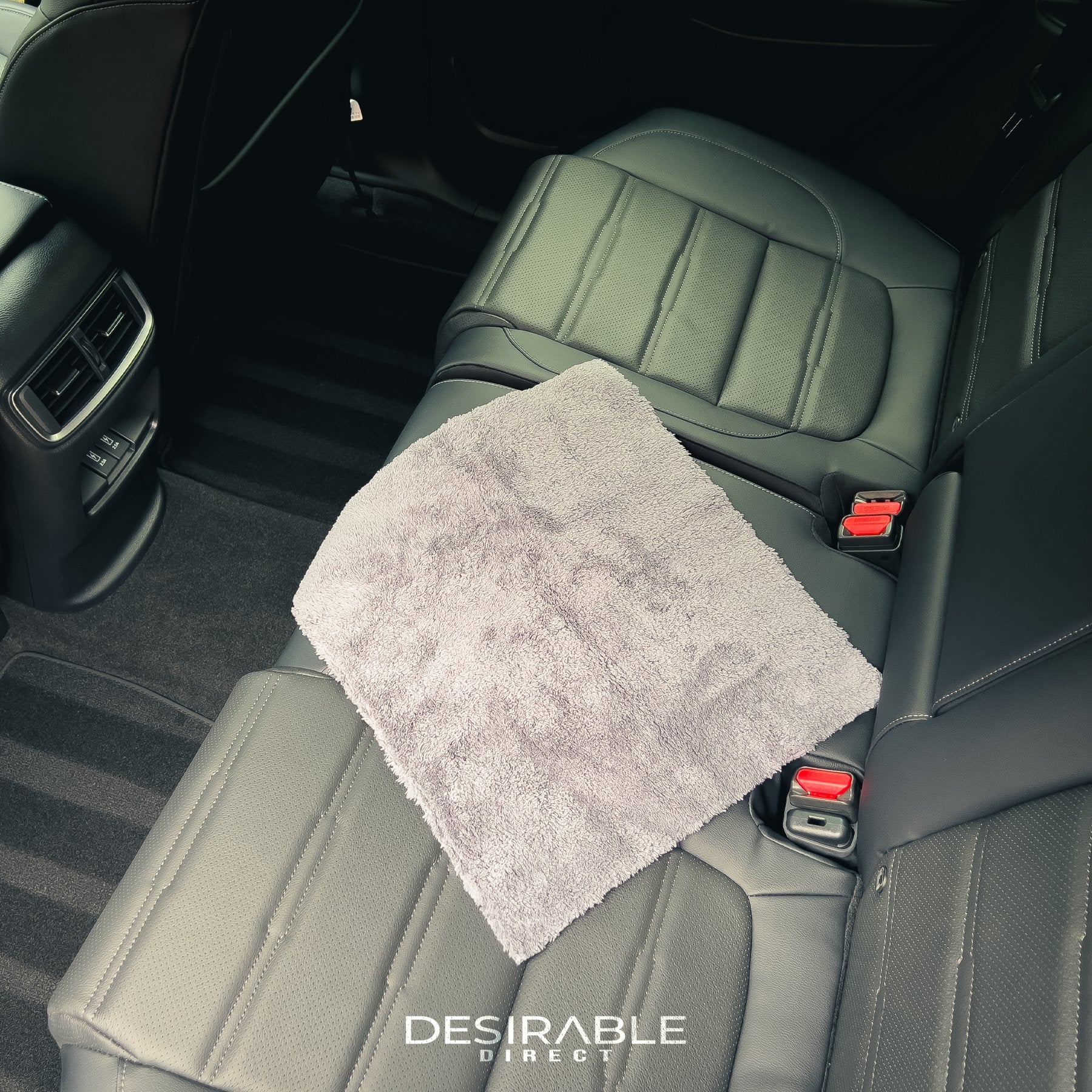 Car care microfibre plush cloth displayed on the back leather seats of a grey car.
